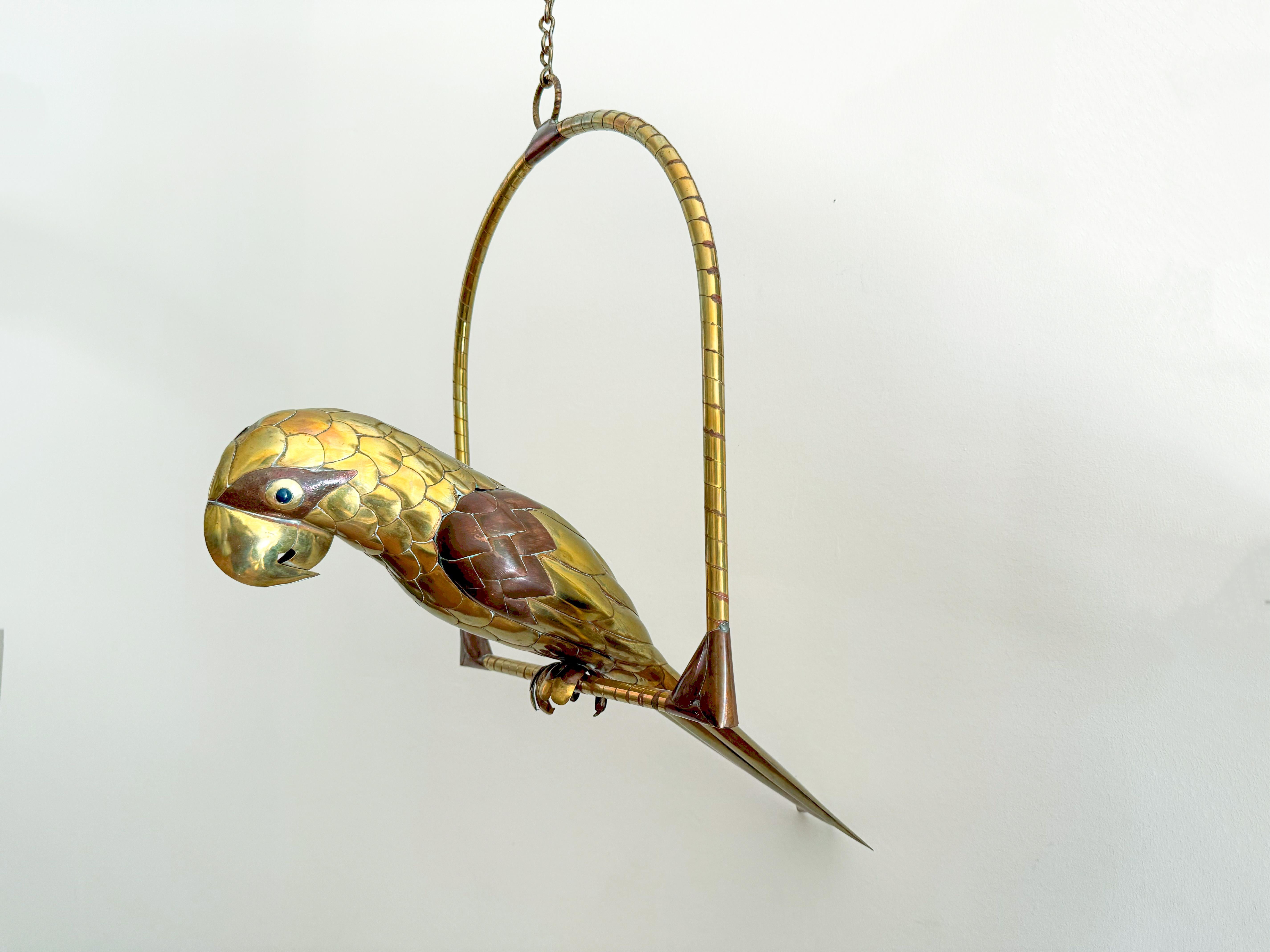 Large, life-size brass and copper Sergio Bustamante parrot on a hanging perch. Crafted in Mexico during the 1970s, it showcases exceptional artistry in brass and copper. Its lifelike details and vibrant presence make it a standout piece for any