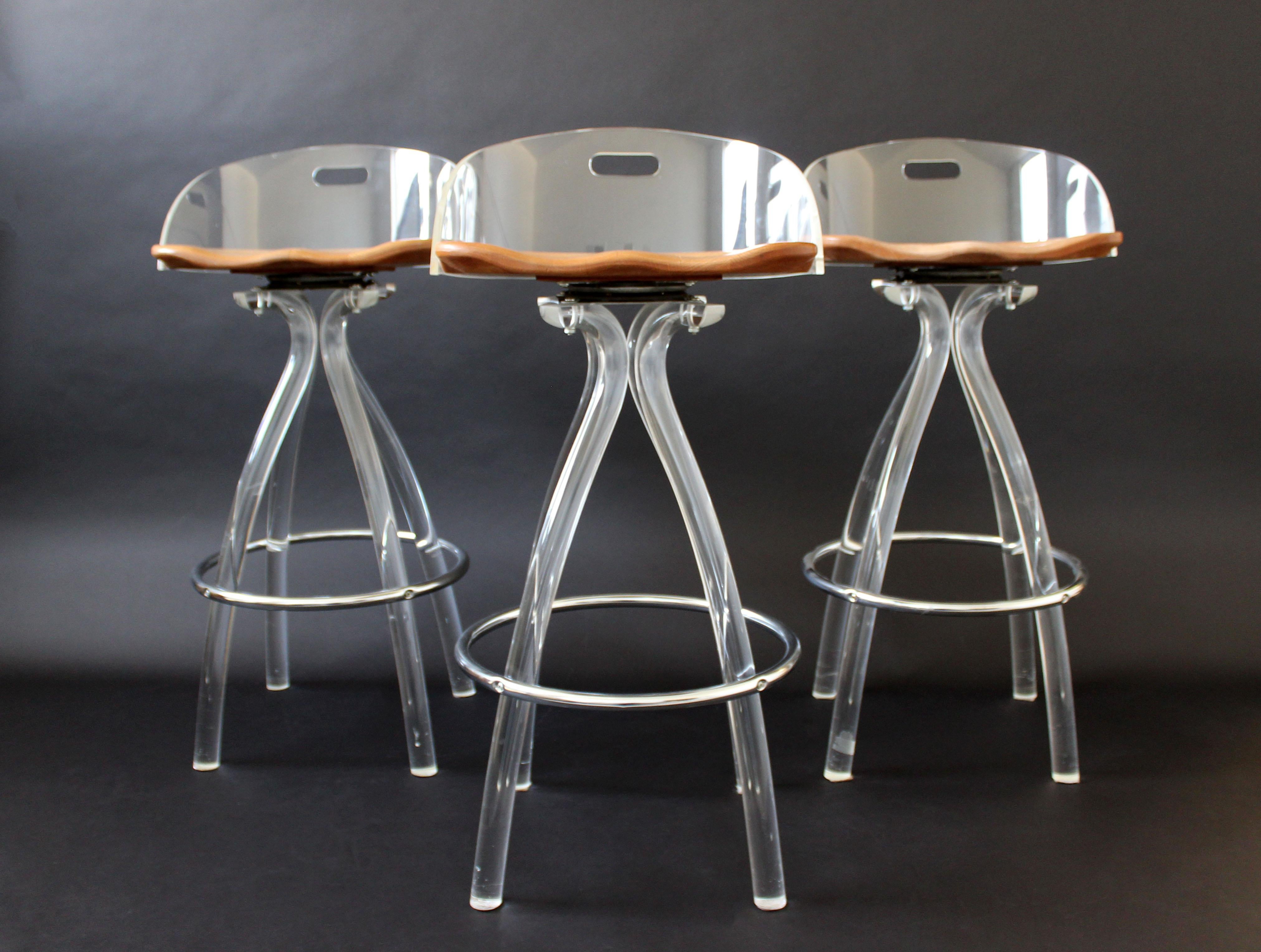 For your consideration is a spectacular set of three bar or counter stools, made of clear Lucite, with wooden saddle seats and steel footrests, by Hill manufacturing, circa 1970s. In very good condition. The dimensions of each are 17.5