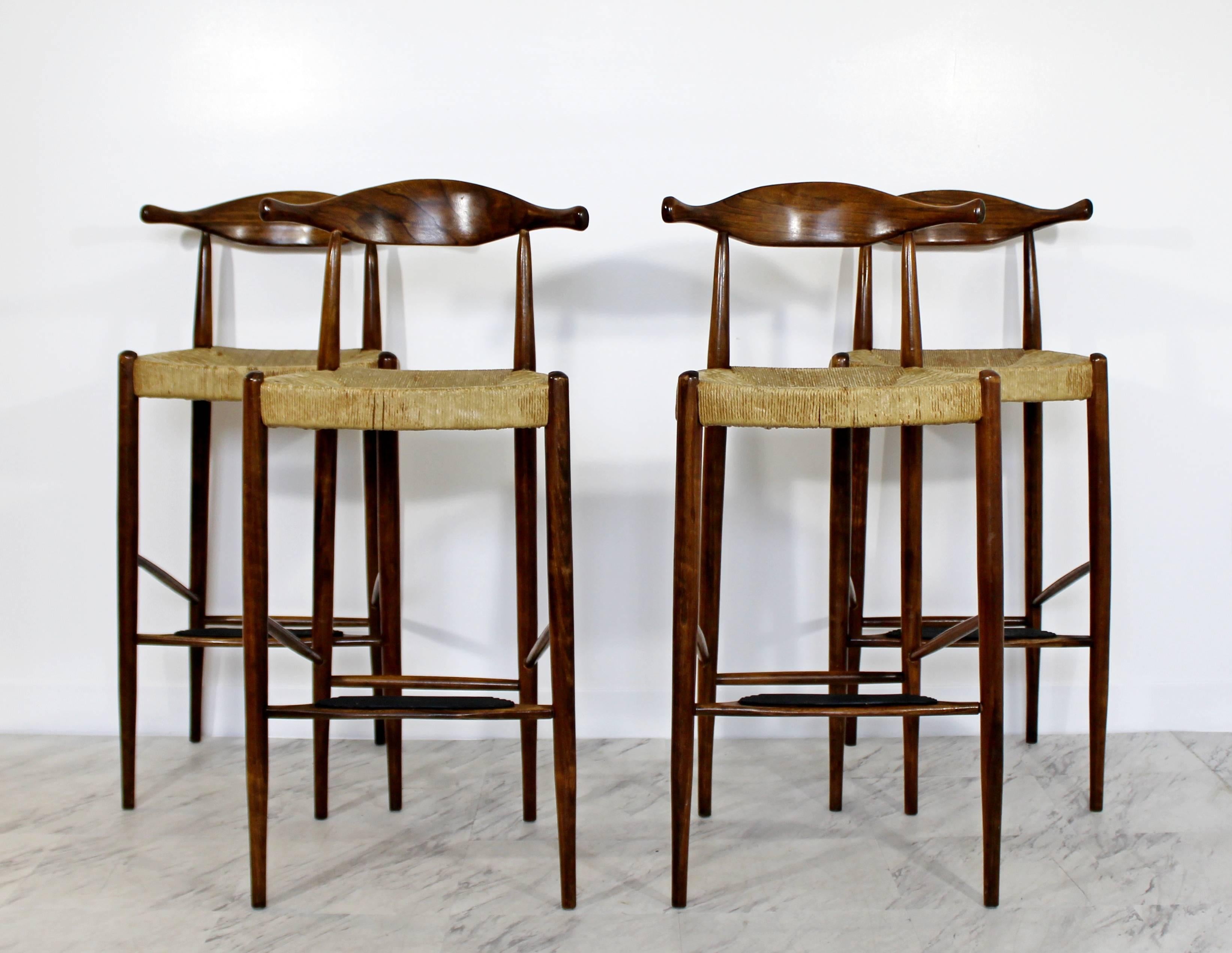 For your consideration is a wonderful set of four wicker rattan rush and teak wood bar stools, with curved backs, circa 1960s. By Hans Wegner called the horn stools. In good condition. The dimensions are 17