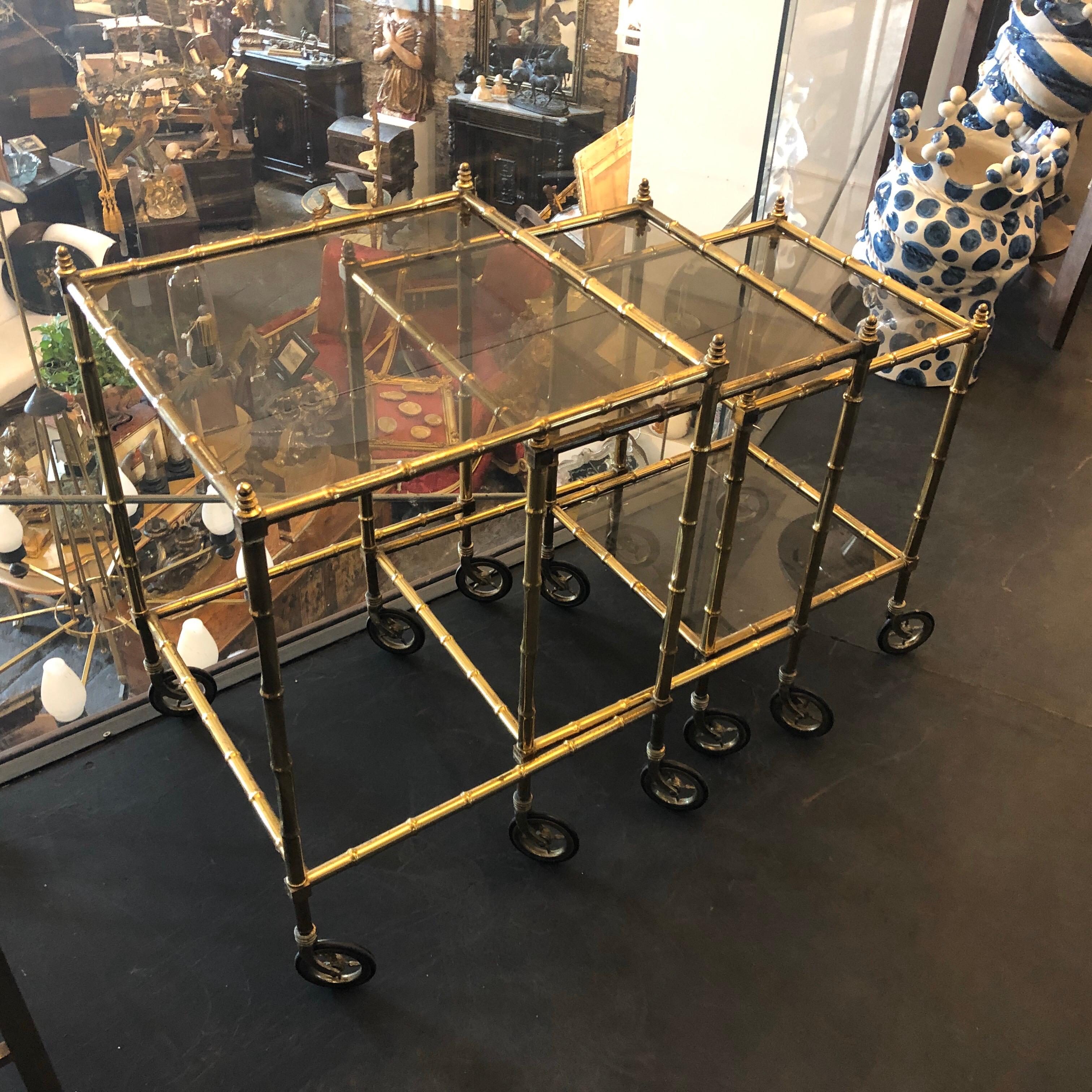 Set of three fake bamboo brass nesting tables made in Italy in the 1960s, brass in original patina and smoked glasses are in perfect conditions. The Nesting Tables are a highly desirable and visually striking collection of furniture. These tables