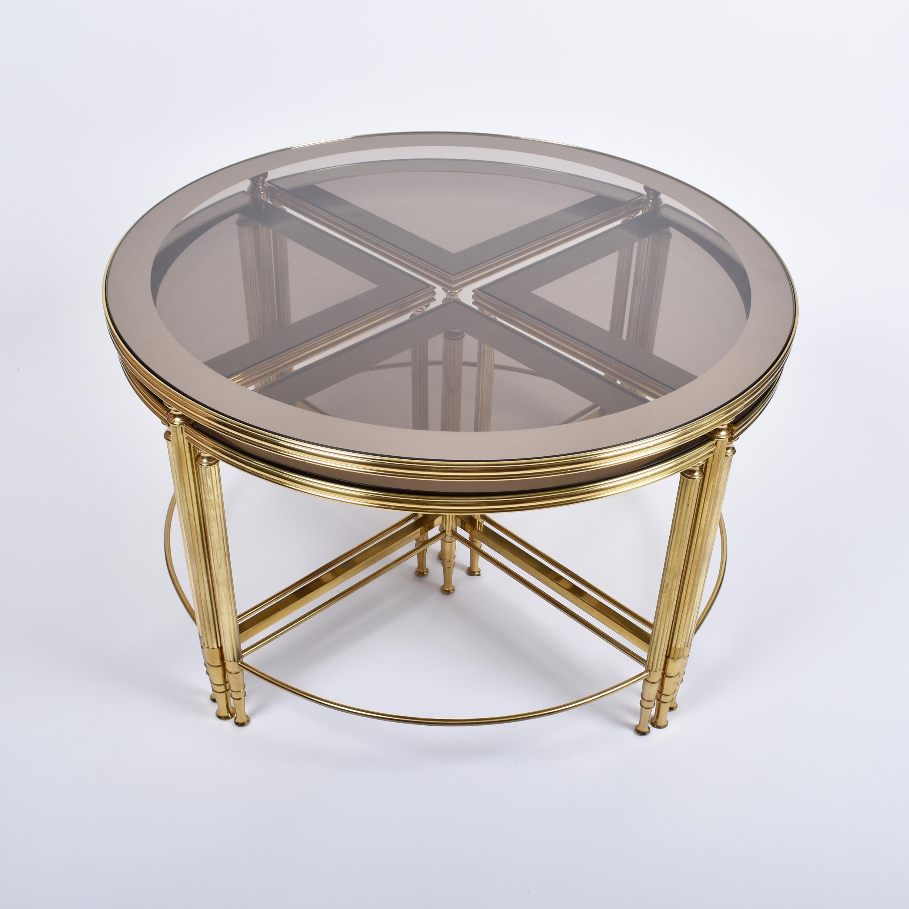 Mid-Century Modern set of five brass and glass coffee tables, in excellent condition.
Elegant ensemble of nesting tables, composed of one main round and four smaller quarters.
The glass top is lightly smoked and mirrored on the sides.
The brass