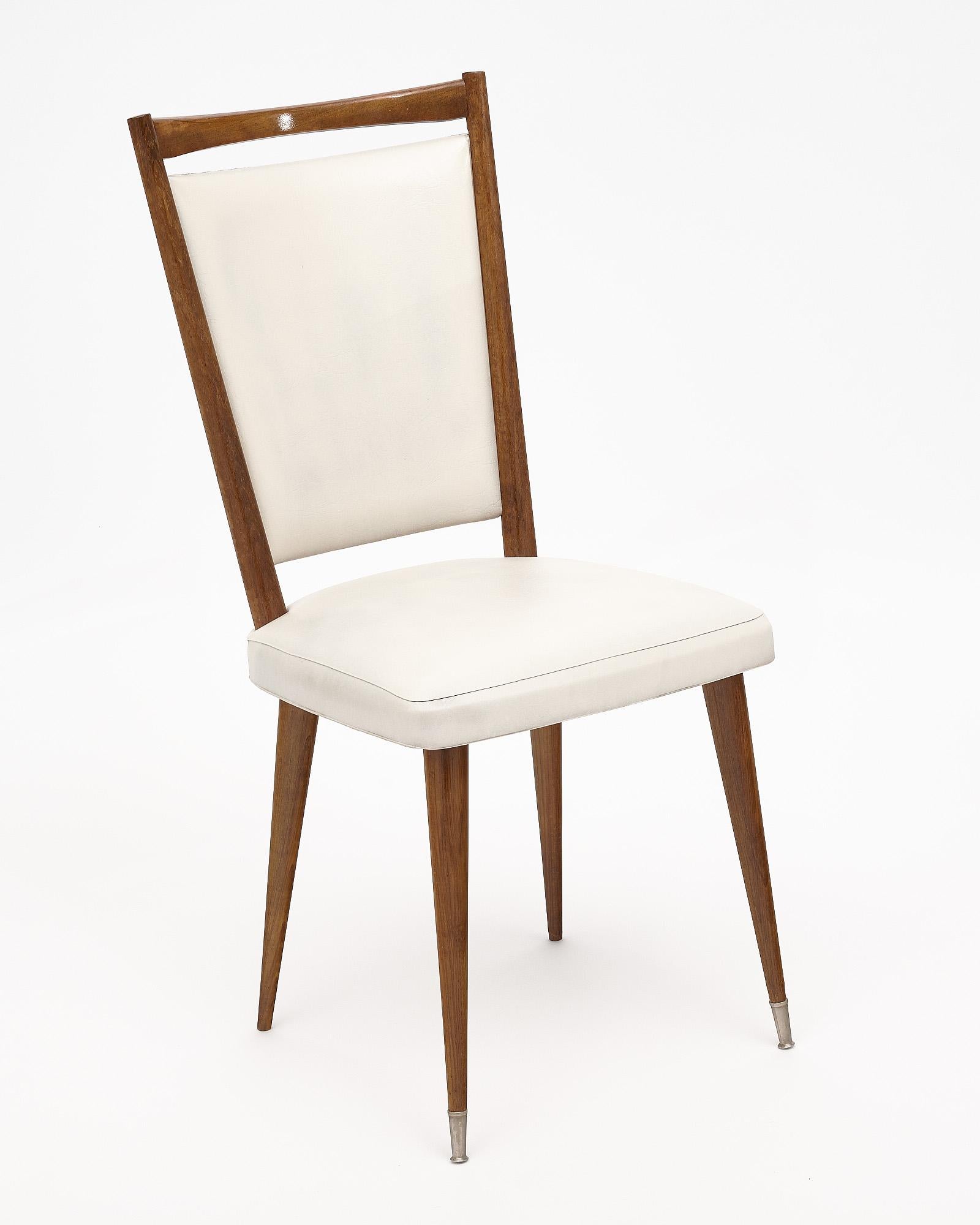 Set of six mid-century dining chairs with a beautiful warm wood structure and white vinyl upholstery. They are supported by tapered legs with brass capped front feet.
