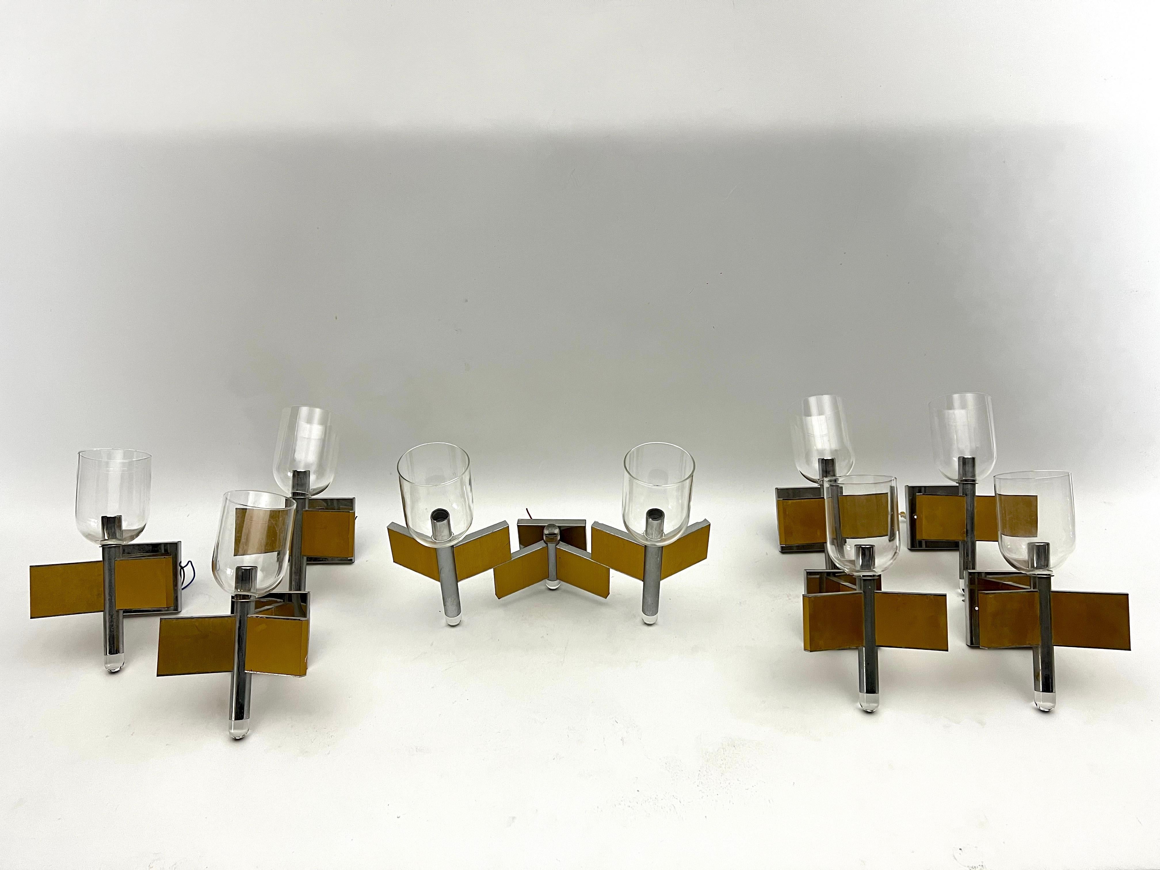 Set of eight sconces in brass, chrome and clear glass signed by Sciolari. The set is composed of one large sconce with double glasses and lights and seven sconces with single glass and light. Fair vintage condition with trace of age and use. No