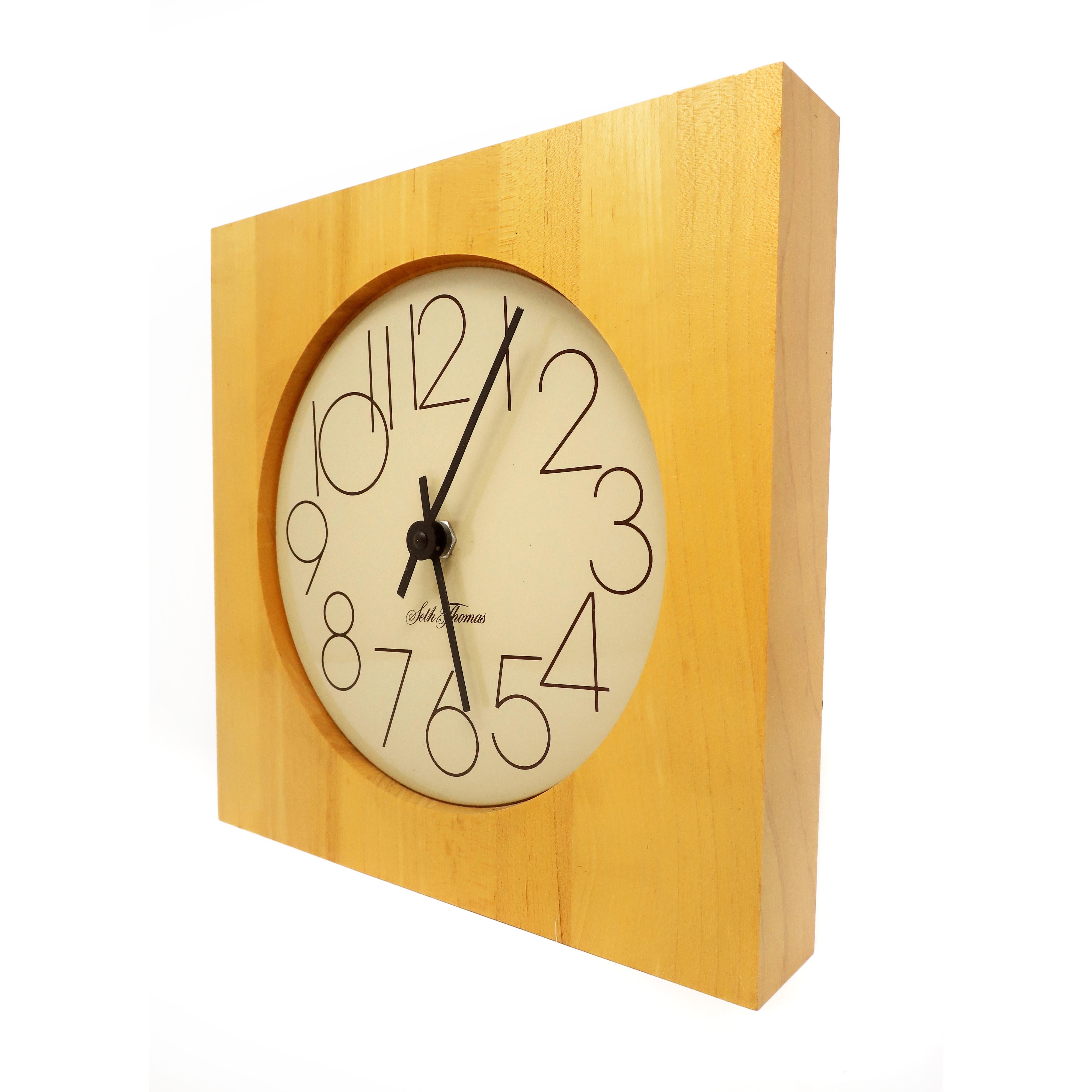 A vintage 1970s Seth Thomas wall clock with round off-white enameled metal face, black hands, and light colored butcher block-style square wood case. In excellent condition with no signs of wear or use and original label on back. Keeps time