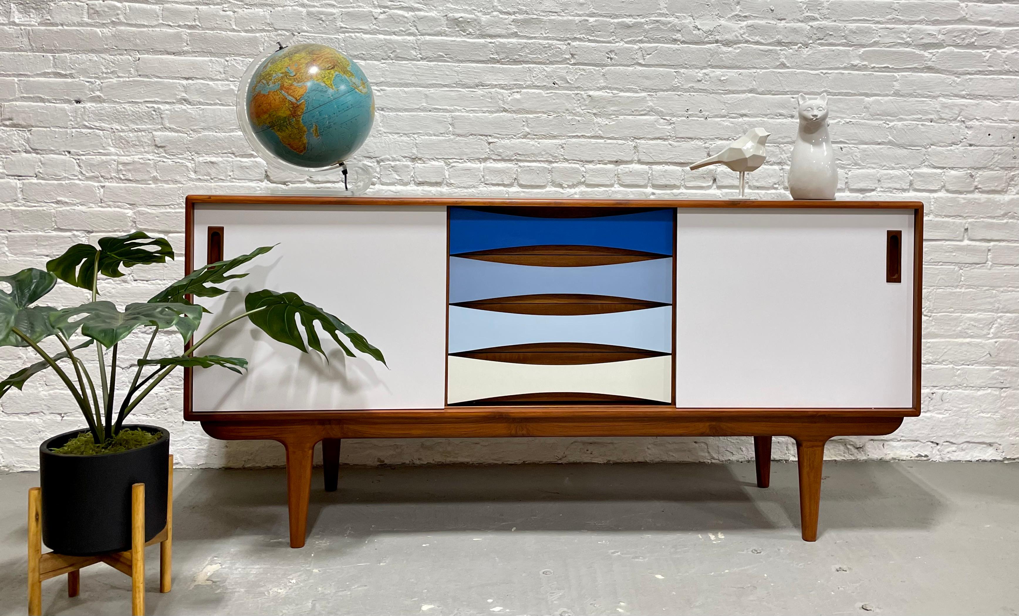 Our Mid-Century Modern styled HANDMADE “Shades of Blue” credenza offers a stunning combination of center drawer space and adjustable shelving along each side. This gorgeous piece is finished with thin sheets of colored laminate over solid wood –