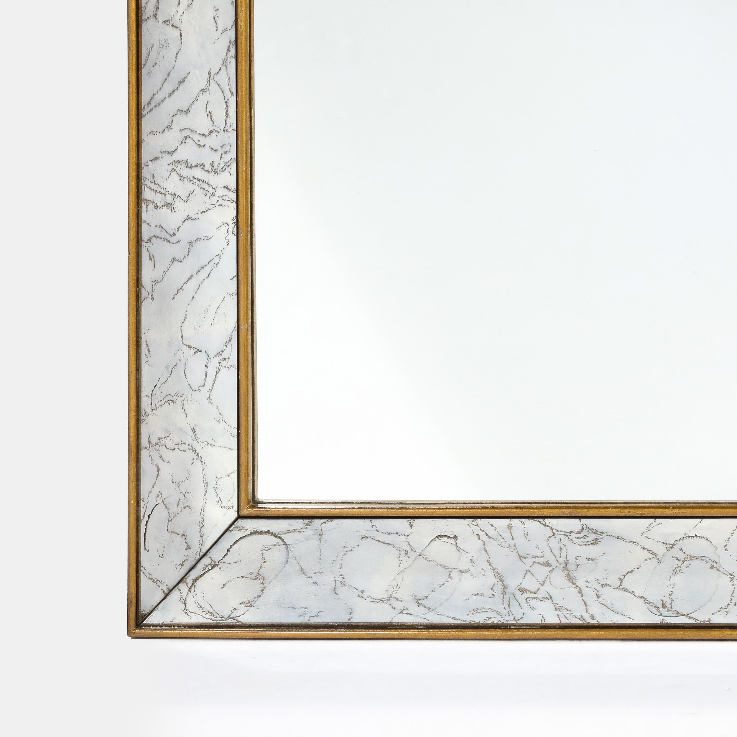 This stunning Mid Century Modern shadowbox mirror was realized in the United States circa 1950. It features a rectangular form with a gilded perimeter in 24kt yellow gold, as well as a gilded interior edge that bookend a beautifully marbled mirror