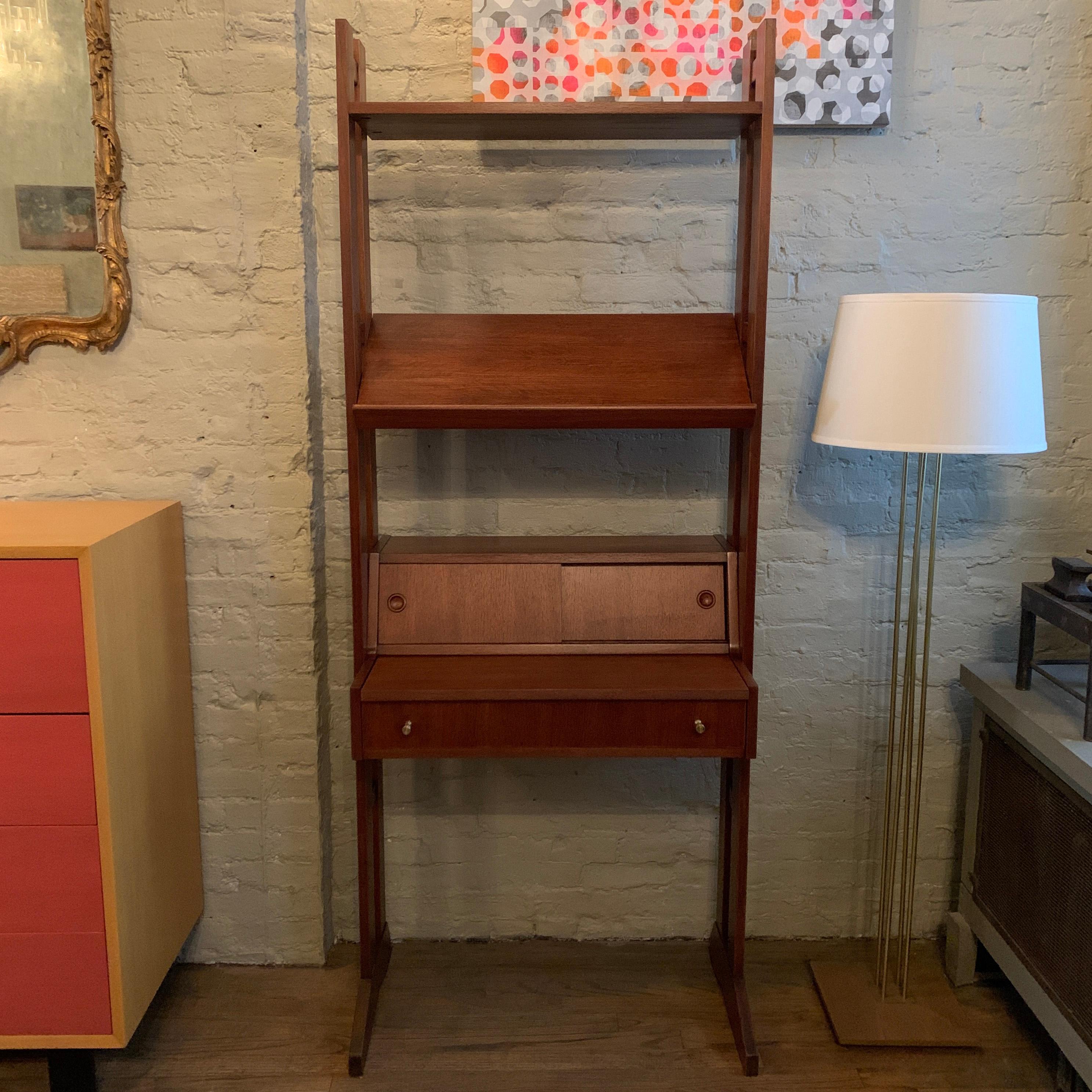 Mid-Century Modern, walnut standing shelf unit with pull-out desk features one drawer with brass pulls, sliding door storage and display rack. The desk pulls out to 13.75 inches D x 26 W.