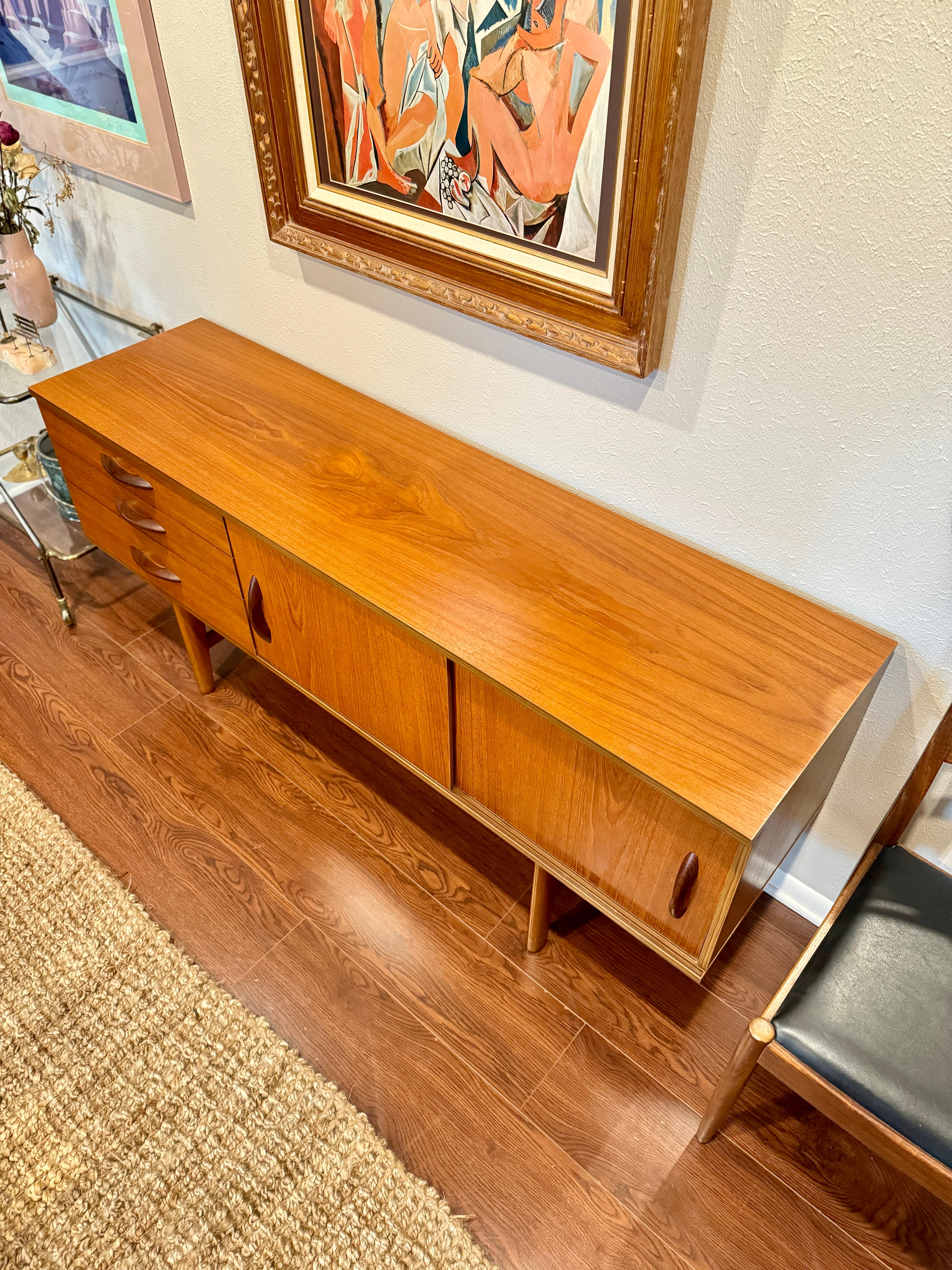 Mid century modern sideboard by Avalon, circa 1960s. This is a fine example of Avalon design, a small sideboard with clean lines and distinctive curved solid teak handles. This piece has sliding doors and plenty of storage space. All drawers open