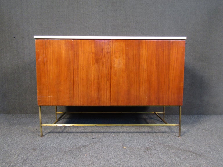 Beautiful Mid-Century Modern design meets timeless craftsmanship in this vintage sideboard by Paul McCobb. Walnut woodgrain, a white top surface, and metal legs pair tastefully with a clean minimal design that also offers plenty of storage. Please