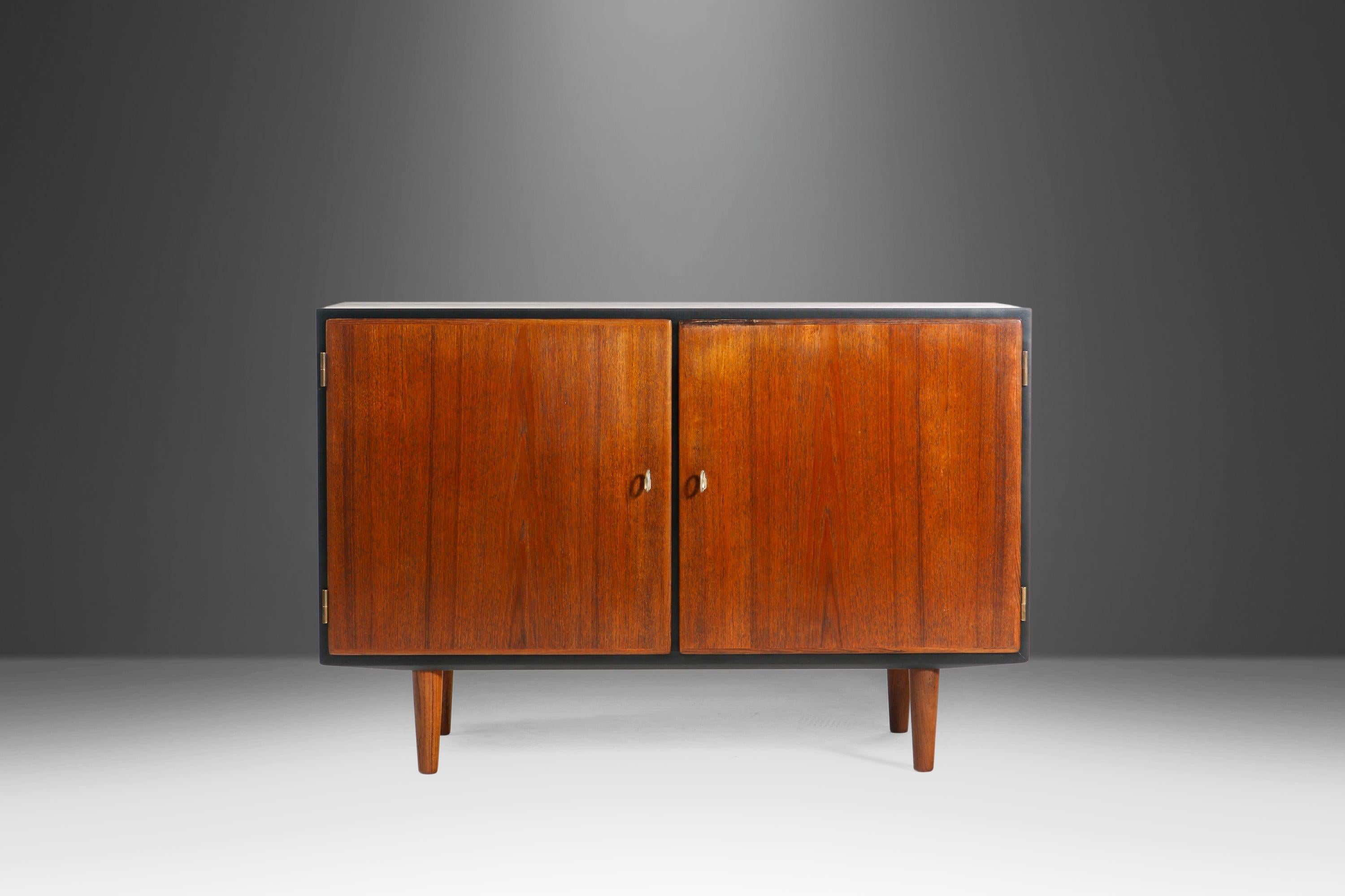 This cabinet is as functional as it is visually striking. Recently restored, this extraordinary sideboard features a newly ebonized frame that perfectly offsets the exceptional teak door faces and legs. Inside there are two adjustable shelves and