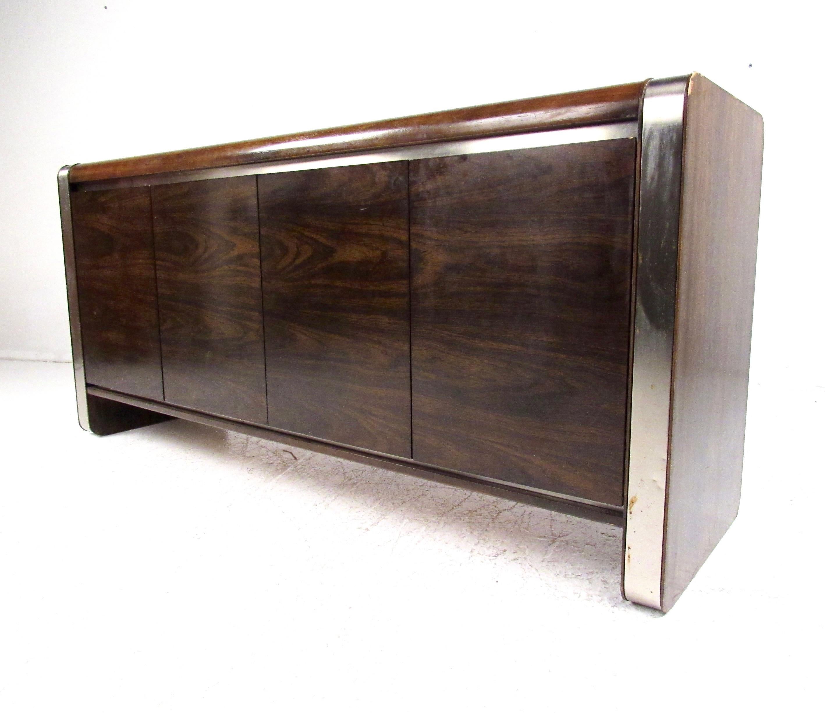 This vintage modern sideboard by Founders Furniture features an exceptional dark walnut finish, perfectly complimented by the steel metal trim. Rounded corners, sleek clean lines, and spacious interior storage make this the perfect addition to