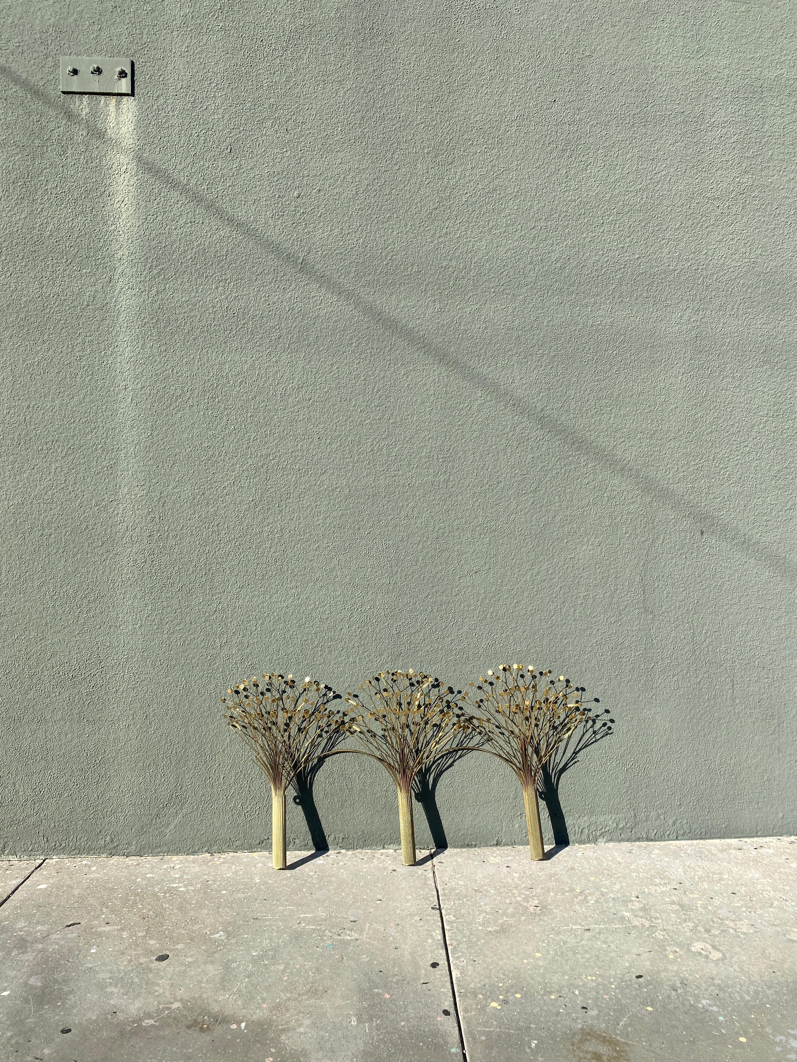 Des tiges en laiton composent trois arbres dont les feuilles en forme de goutte d'eau scintillent sous l'effet de la lumière réfléchie. Chaque 