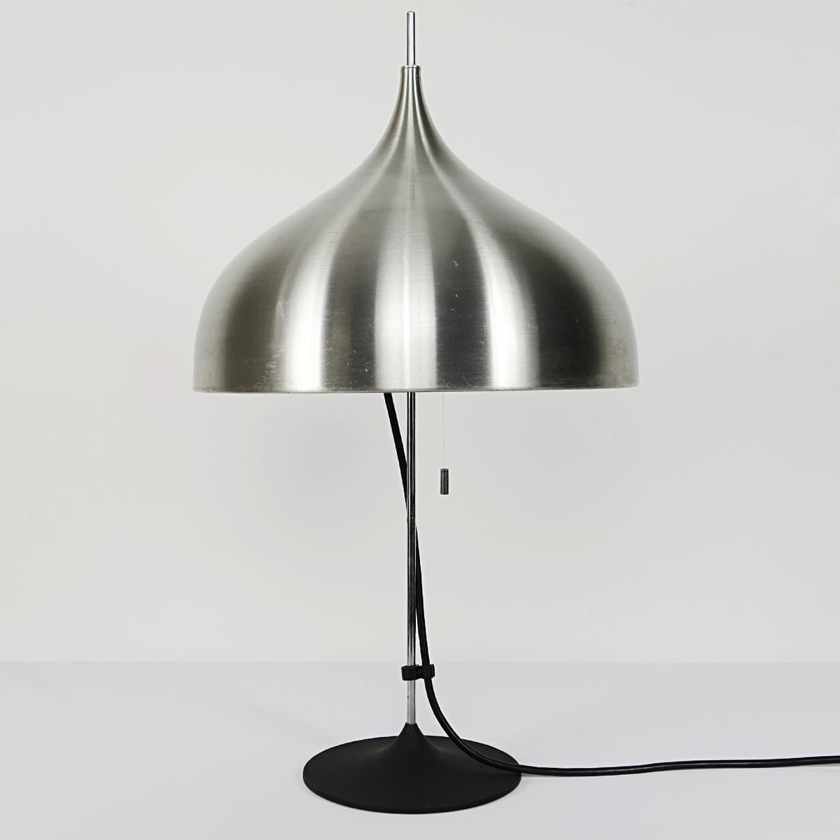 This Mid-Century Modern table lamp was made by Doria. It has a black cast iron foot in the shape of a tulip. The chrome 'bar' carrying the shade is beautifully thin and goes on above the elegantly shaped stainless steel shade.
Contains two light