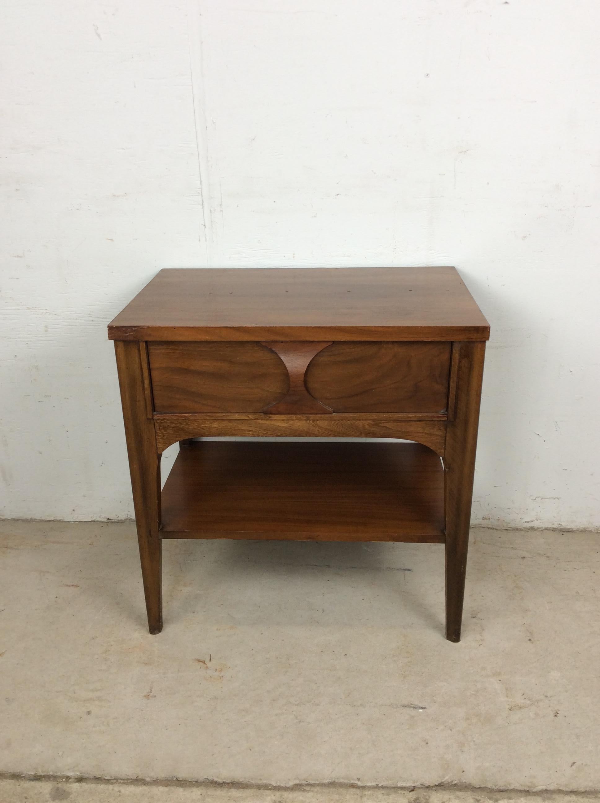 This mid century modern nightstand by Kent Coffey features hardwood construction, walnut veneer with original finish, single drawer with unique bentwood pull, opened storage shelf and tall tapered legs. 

Dimensions: 23w 15d 24h 

Condition notes: