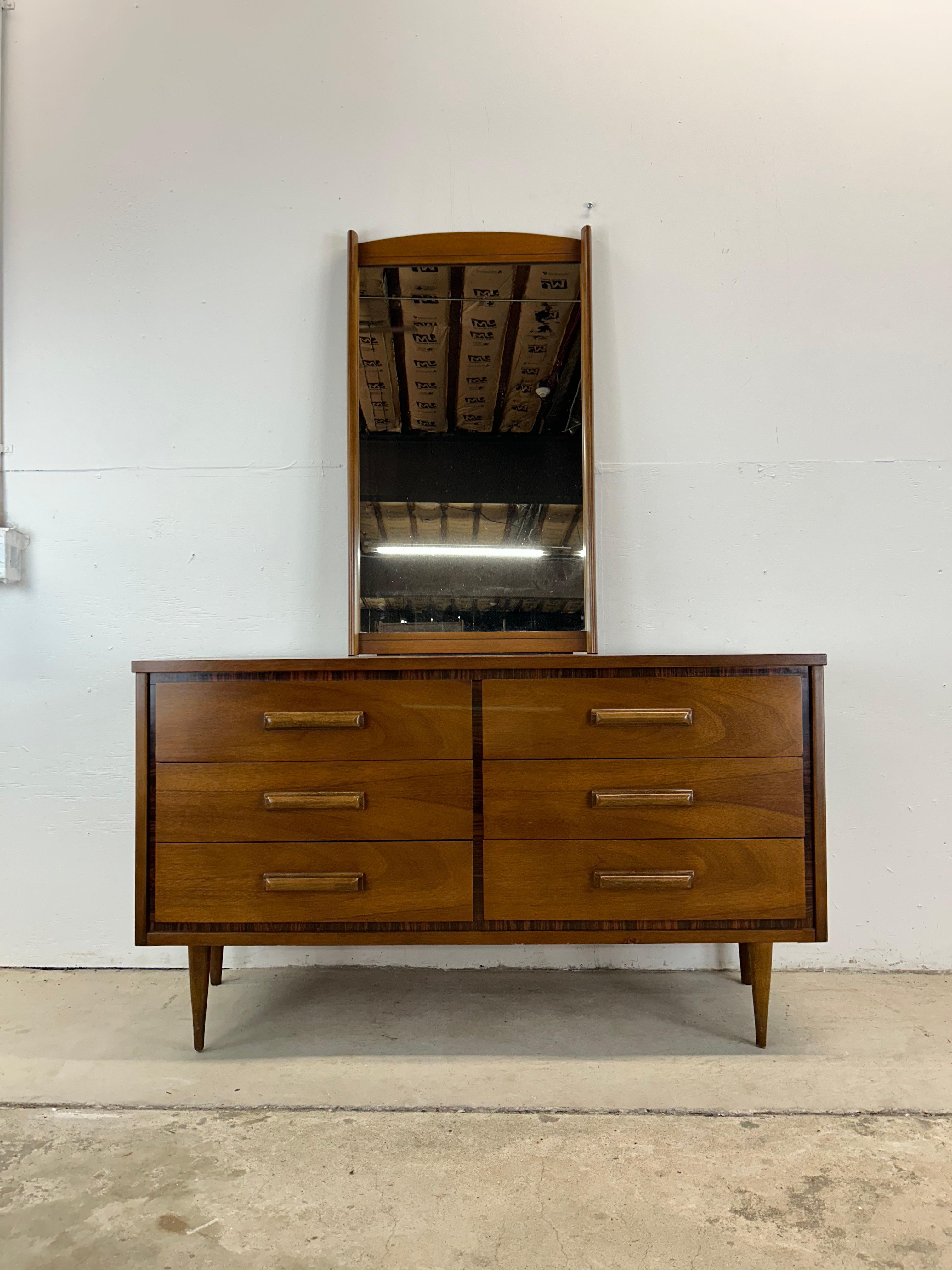 Questo comò basso moderno di Bassett Furniture è caratterizzato da una struttura in legno massiccio, impiallacciatura in noce con finitura originale, sei cassetti a coda di rondine con tiretti in legno scolpito, finiture in palissandro, piano in