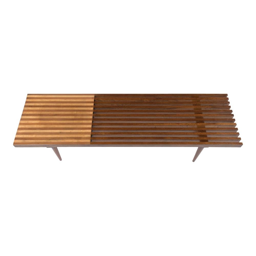 This Mid-Century Modern slatted bench has been recently restored and has its natural wood color with a beautiful polished finish. The bench is made out of walnut, and maple wood combination with a solid wood seat on the side and design. The bench