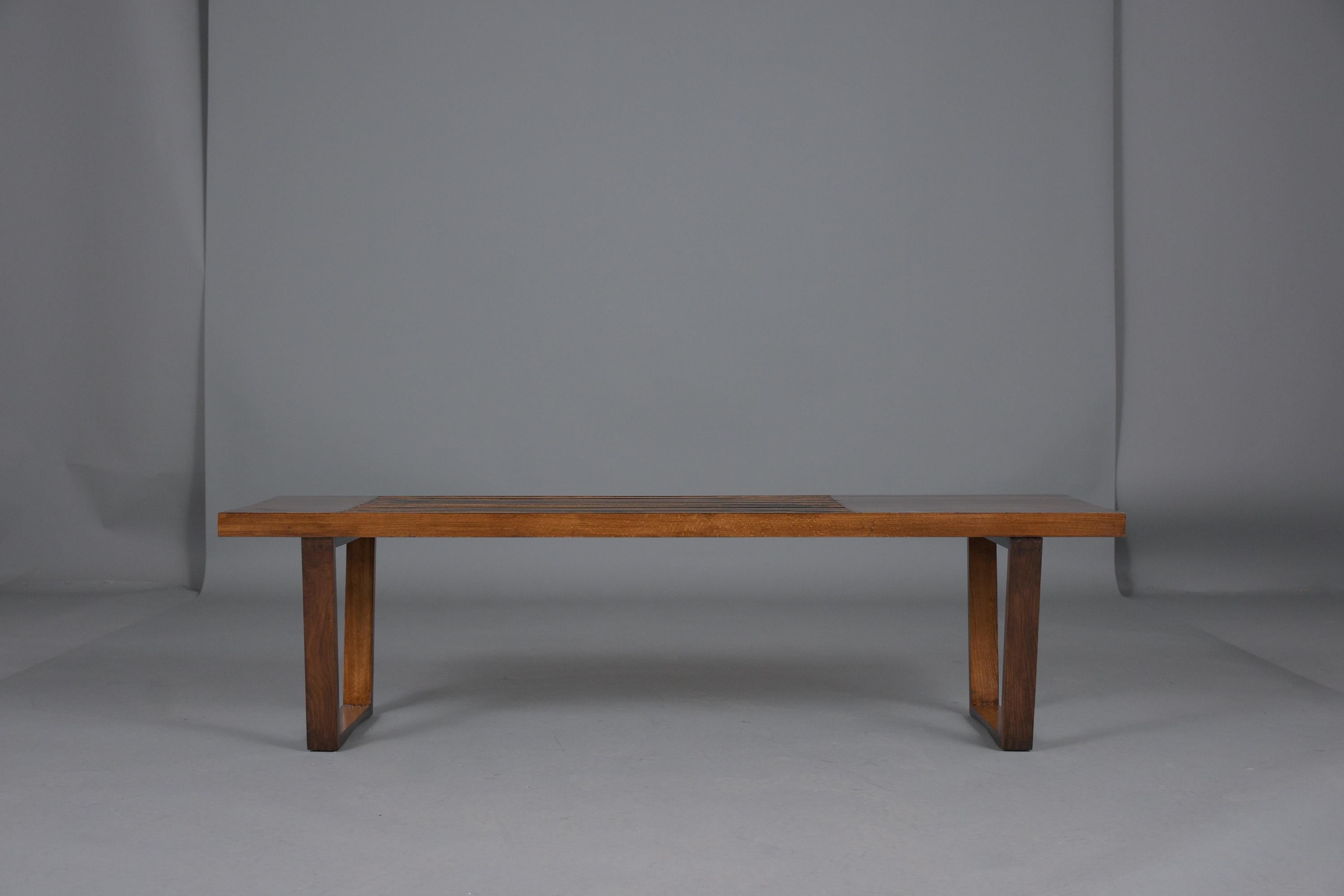 This sleek mid-century modern slatted bench in the style of George Miller is handcrafted out of beechwood and has been professionally restored by our team of craftsmen. The bench is newly finished in medium and dark walnut color with a beautiful