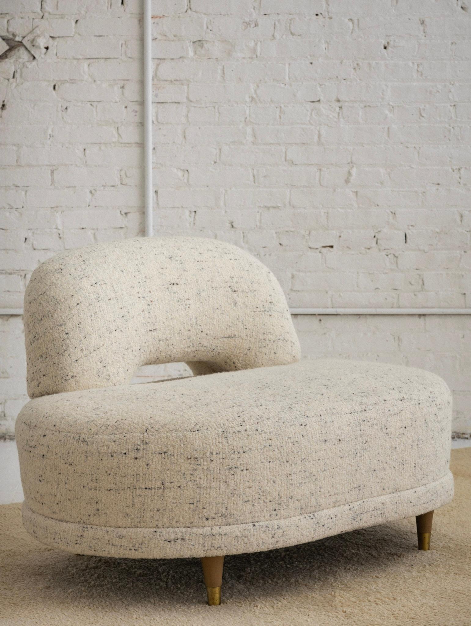 A Mid-Century Modern slipper lounge chair. Newly reupholstered in a soft textured wool. Cream in color with speckles of brown and black. Blonde wood feet with brass caps.