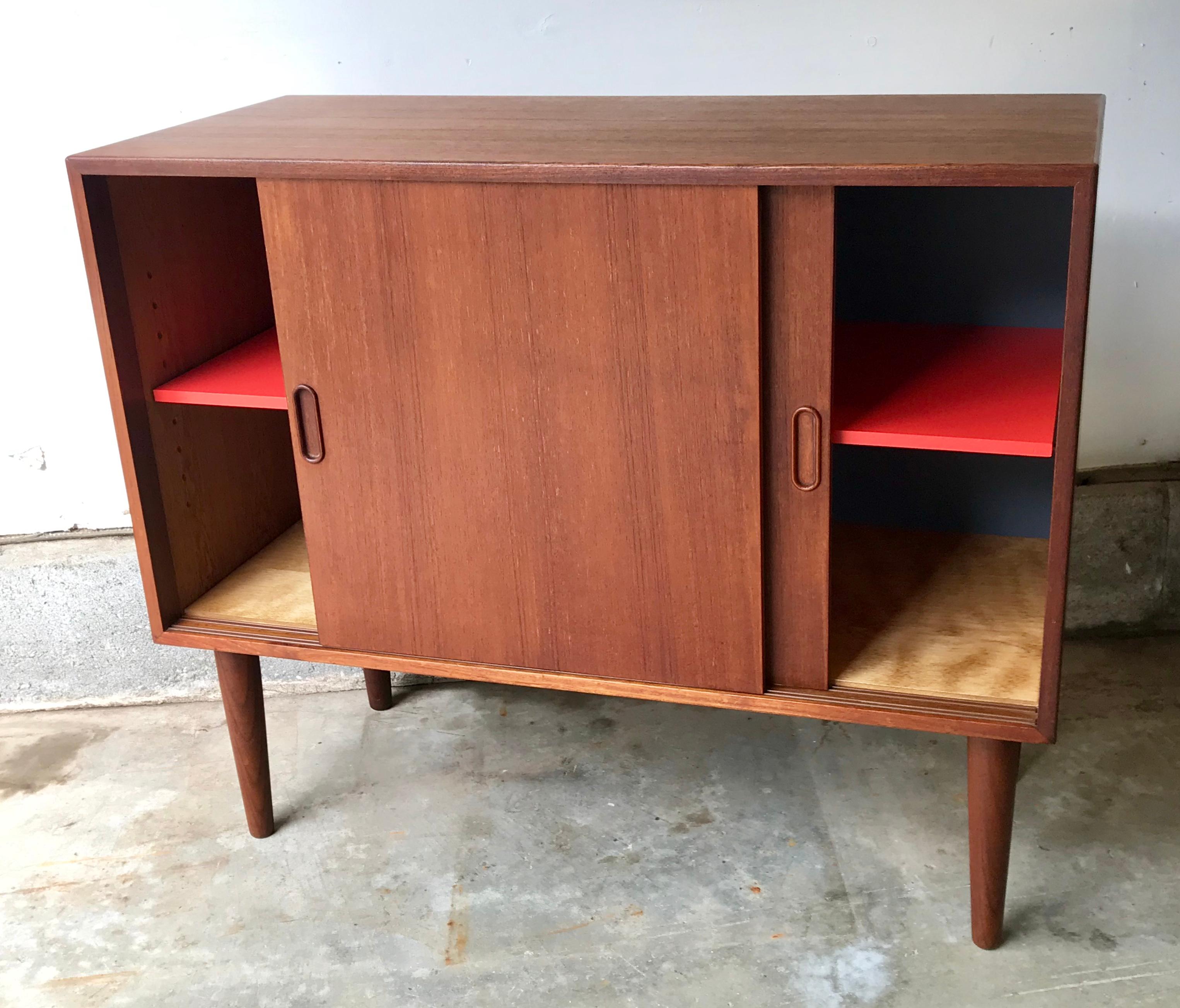 Very nice smaller scale teak credenza or storage cabinet, sliding doors with adjustable shelf. Professionally restored with new bottom and back panel with salsa colored red shelf.