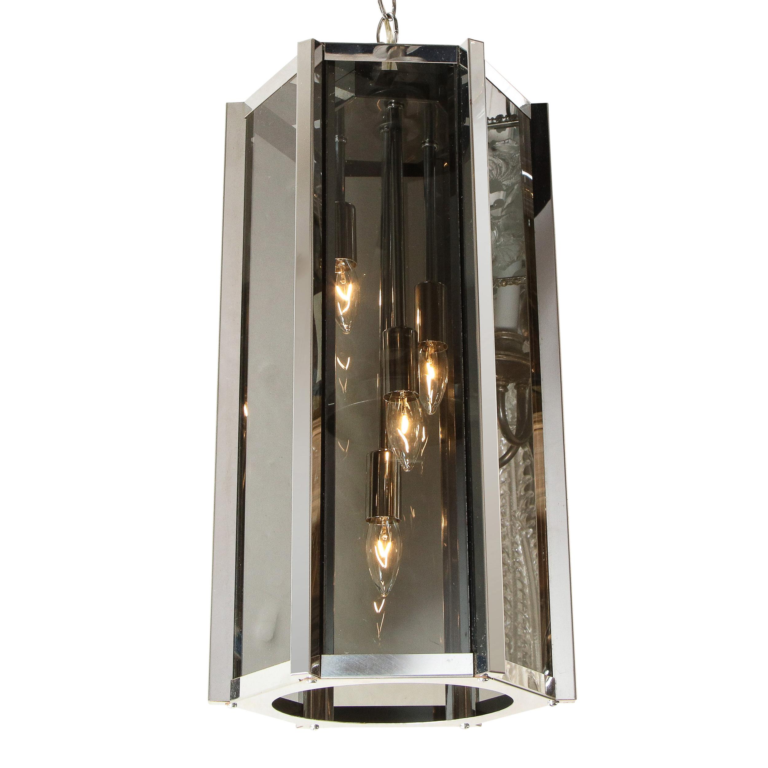 This refined Mid-Century Modern lantern chandelier was realized in the United States, circa 1970. It features a hexagonal body with smoked glass rectangular panels supported by a lustrous chrome frame. With its bold silhouette, clean lines and