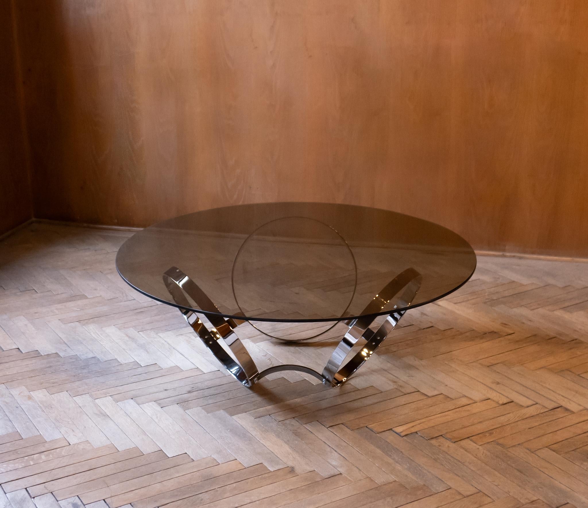 Mid-Century Modern Smoked Glass Chrome Coffee Table, Germany 1970s.

This large round coffee table with its table top made of smoked glass and its scuptural chrome base, reminiscent of the iconic designs by renowned creator Ronald Schmitt,