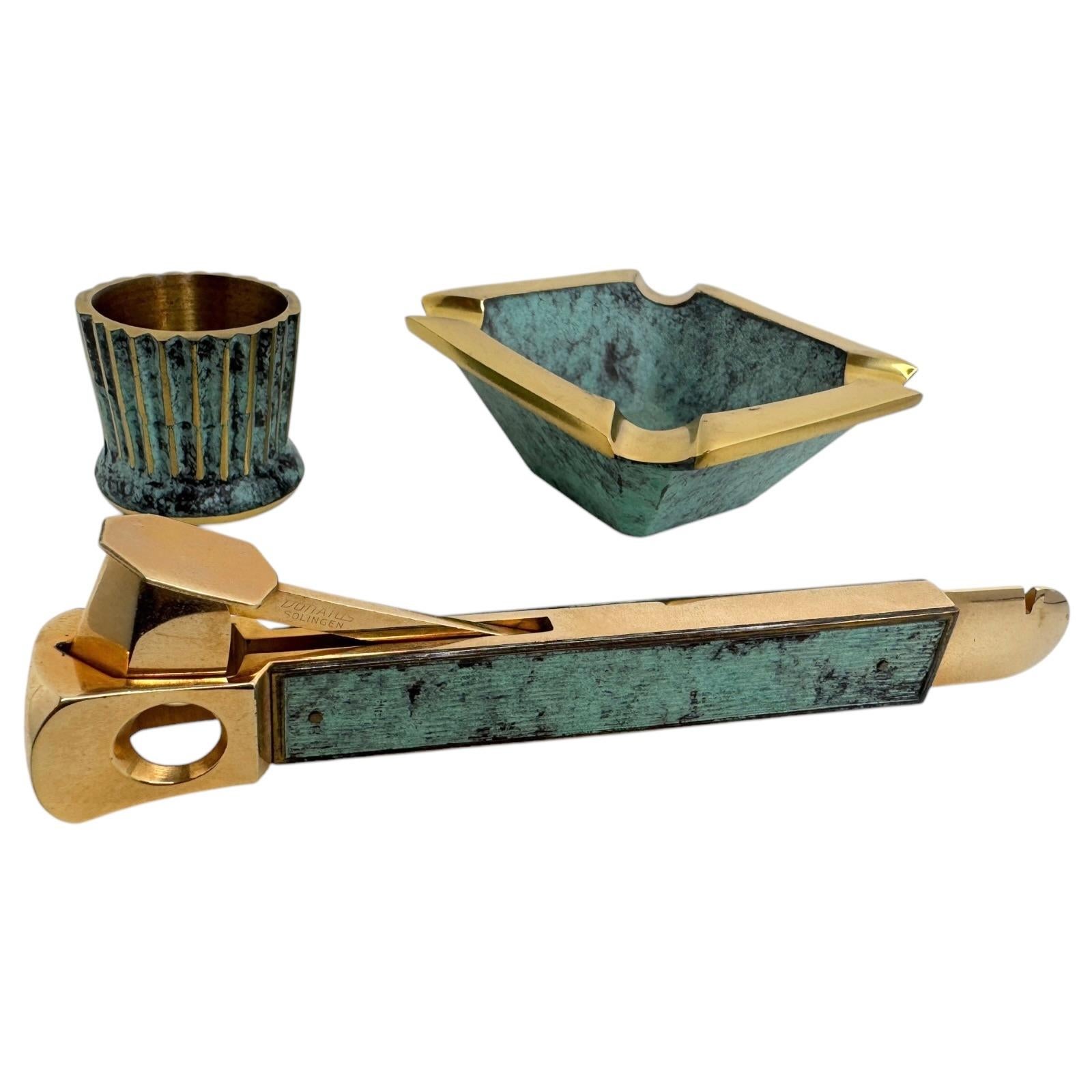 Very attractive set of three tobacco object 1950s to 1960s German. A bronze/brass table set of 4 items, included a cigar cutter, an ashtray and matchstick holder.  Verdigris design with gold-plated elements. Found at an estate sale in Nuremberg,