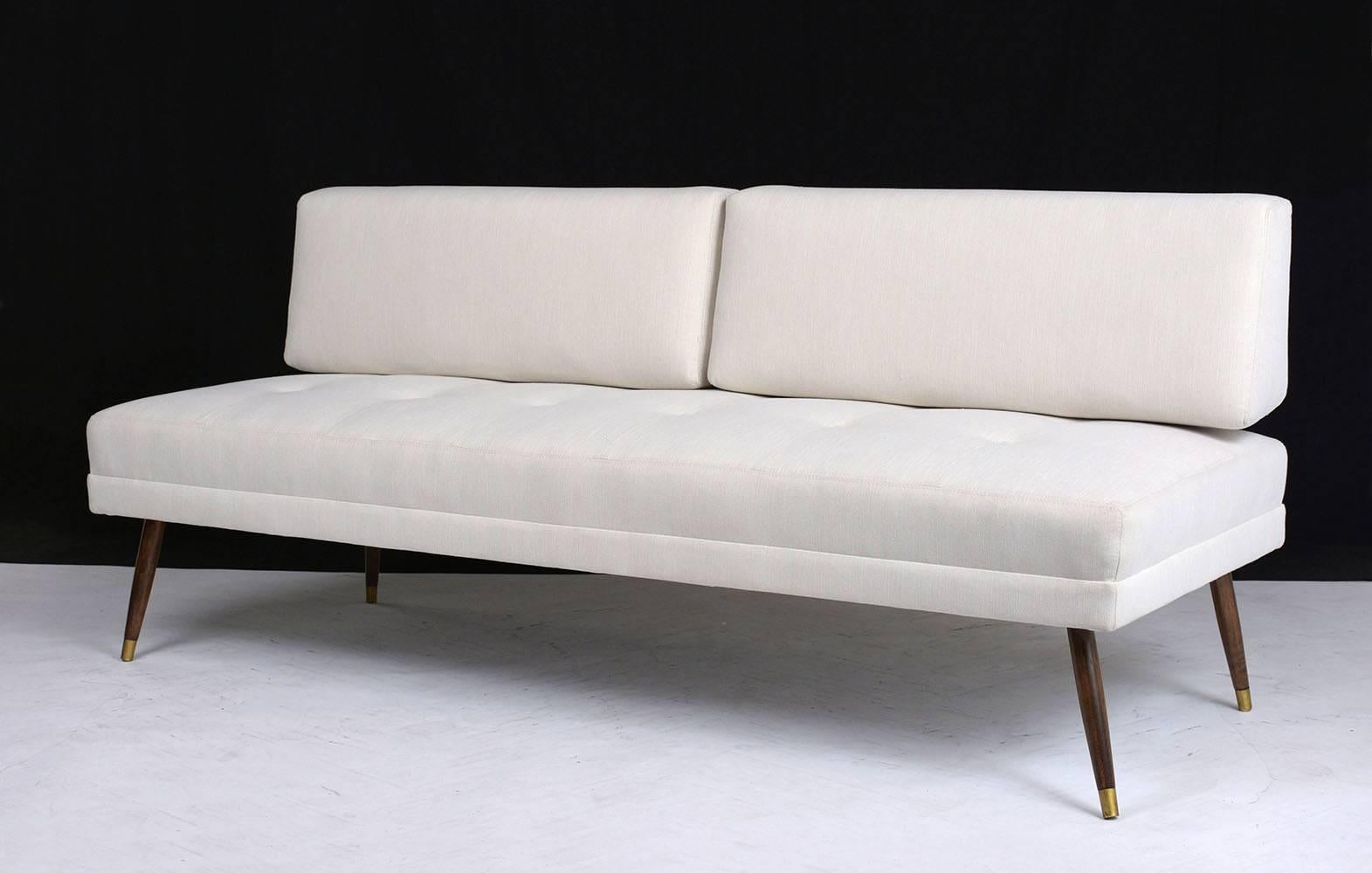This 1960s Mid-Century Modern sofa has been completely restored with comfortable new cushions and upholstery. The sofa is professionally upholstered in an ivory color fabric with double stitching details. The seat cushion is attached with tufted