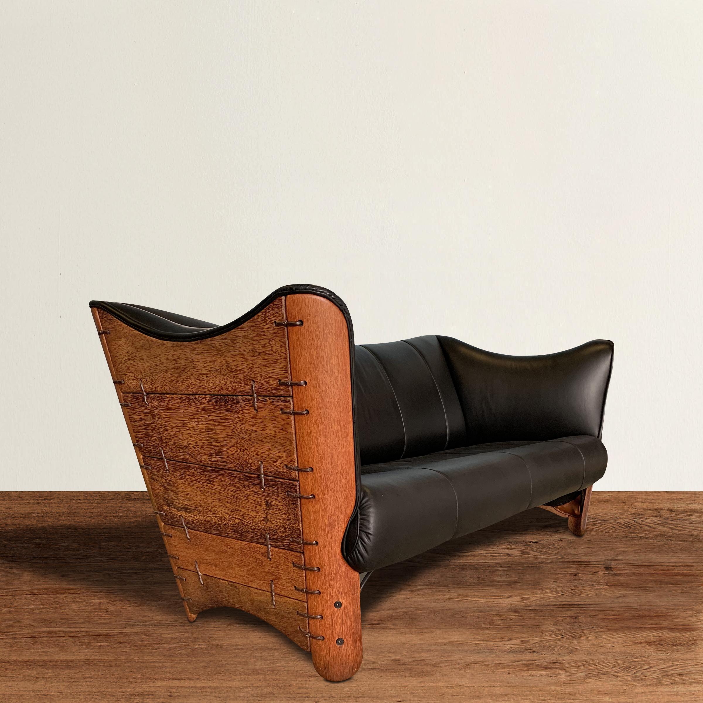 A fantastic modern palm wood sofa constructed of smooth palm wood panels stitched together with leather ties, and upholstered in black leather. The back and sides flare outward and offer a comfortable pitch for reclining. Leather is in perfect