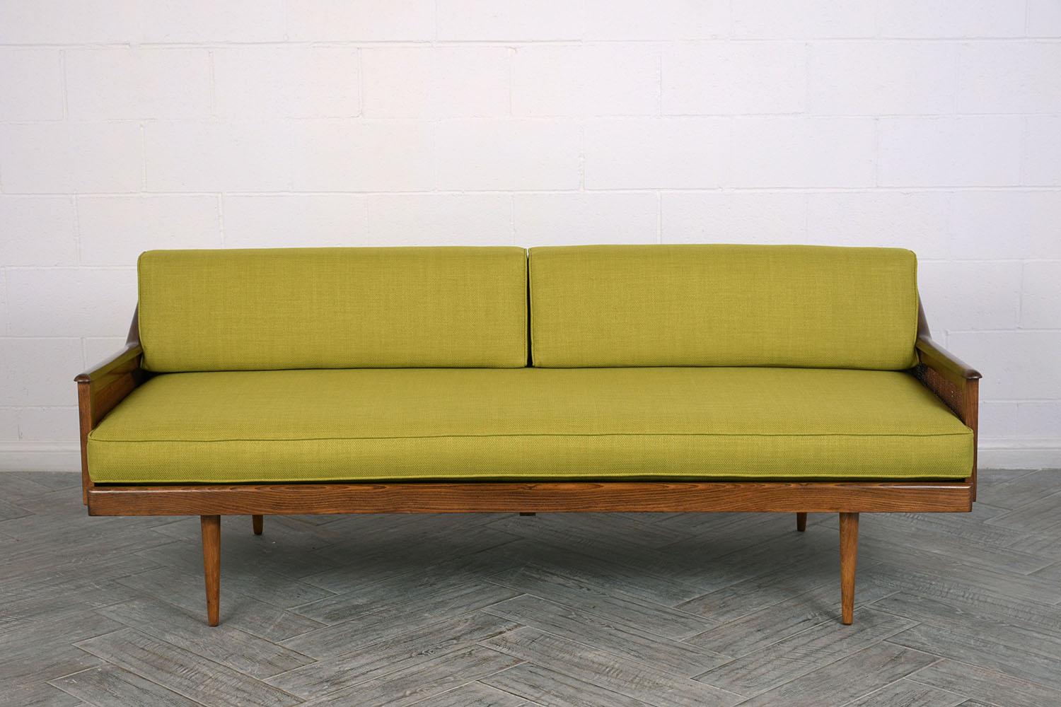 This 1960s Mid-Century Modern sofa has been completely restored. The wood frame has been refinished in a dark walnut color with a lacquered finish. The sides of the sofa have canning inserts and the back has cutout accents. The new foam cushions are