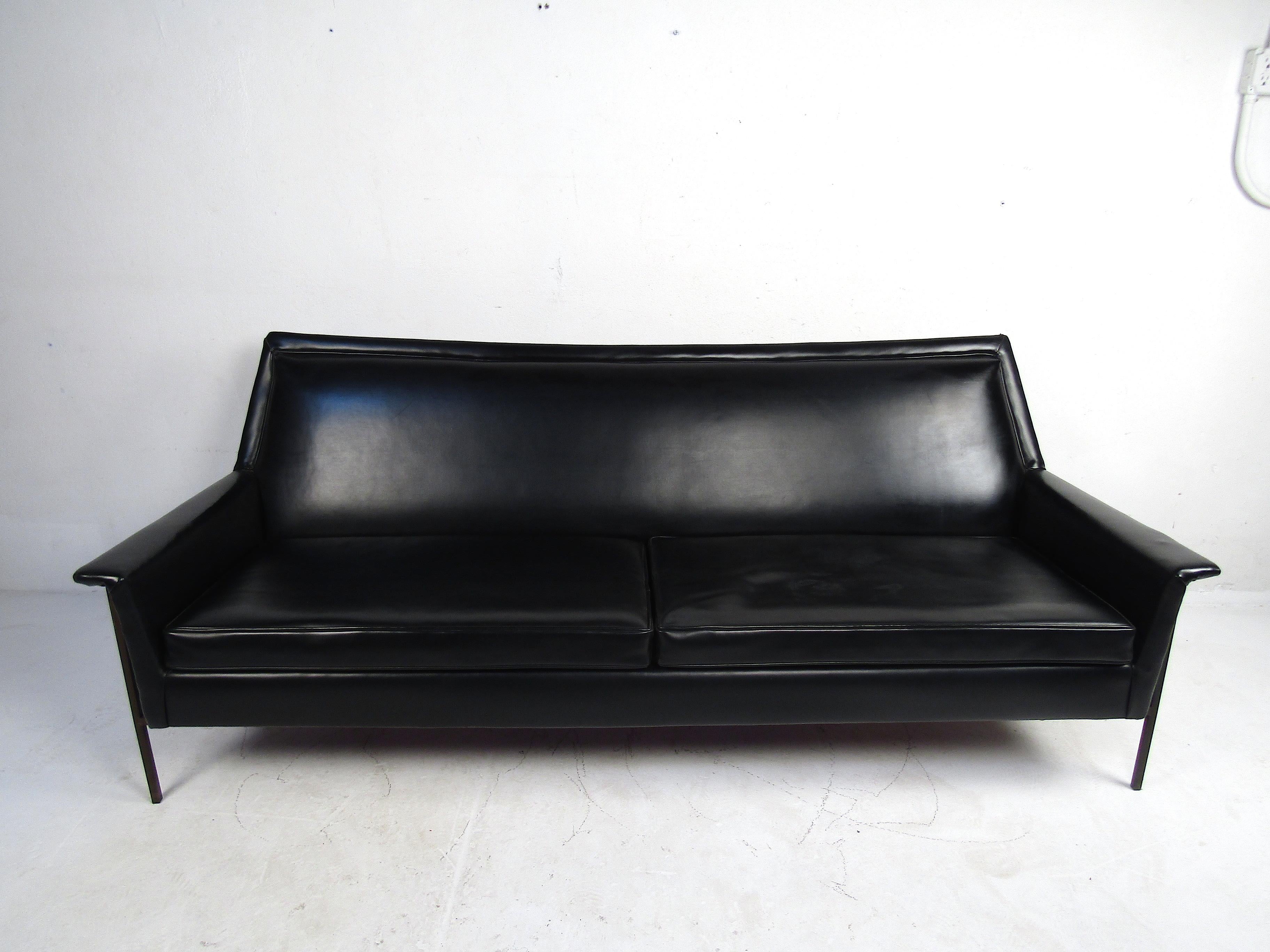 Mid-Century Modern sofa by Harvey Probber. Spacious seating area covered in a vintage black faux-leather upholstery. Sturdy brass frame with matching decorative nails lining the corners of the piece. This sofa would make a great centerpiece for any