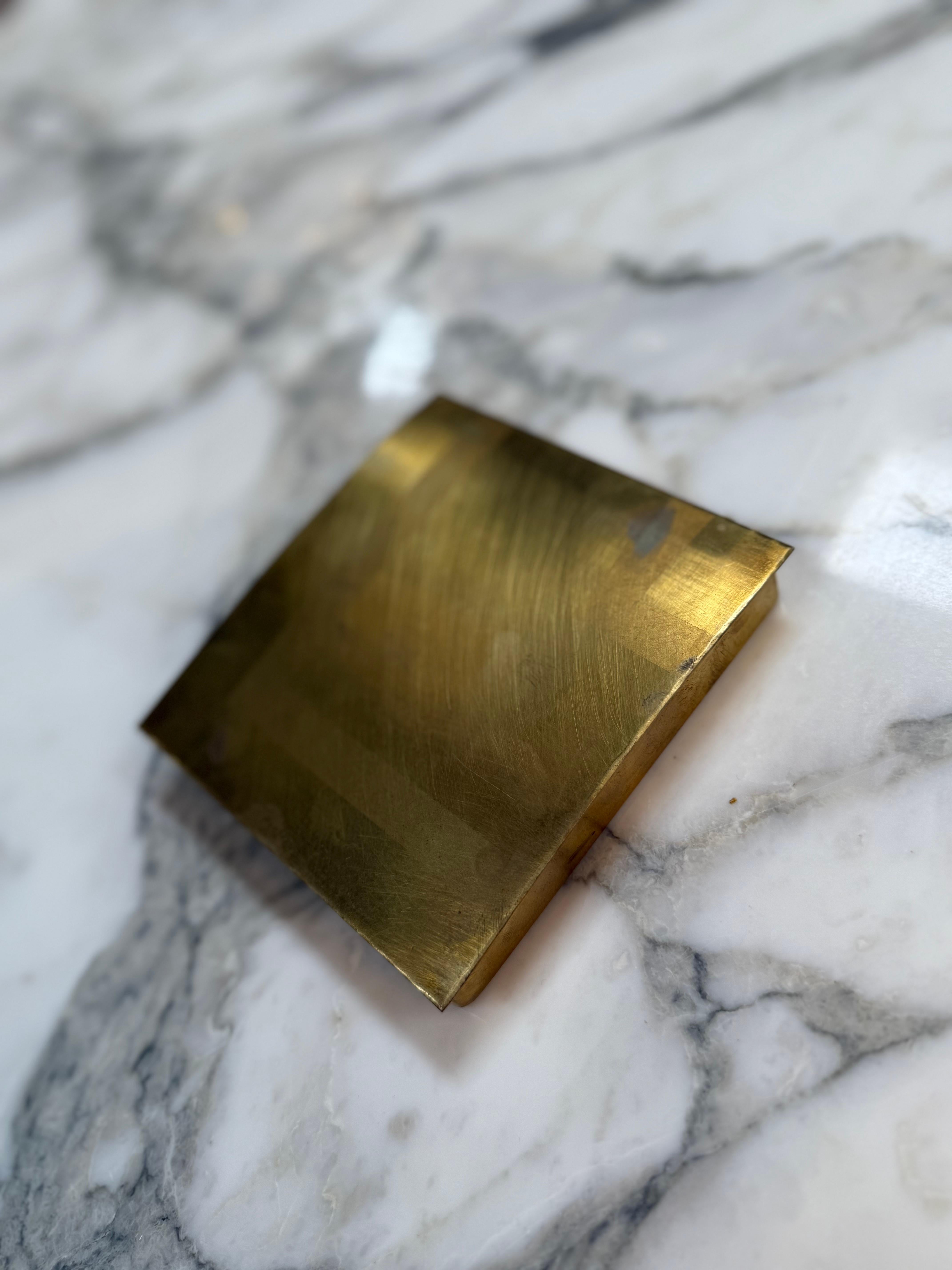This rectangular mid-century modern box is crafted entirely from solid brass, featuring a brushed satin finish that gives it a warm, understated sheen. The box has a slightly curved lid and clean, minimalist lines — a hallmark of mid-century design