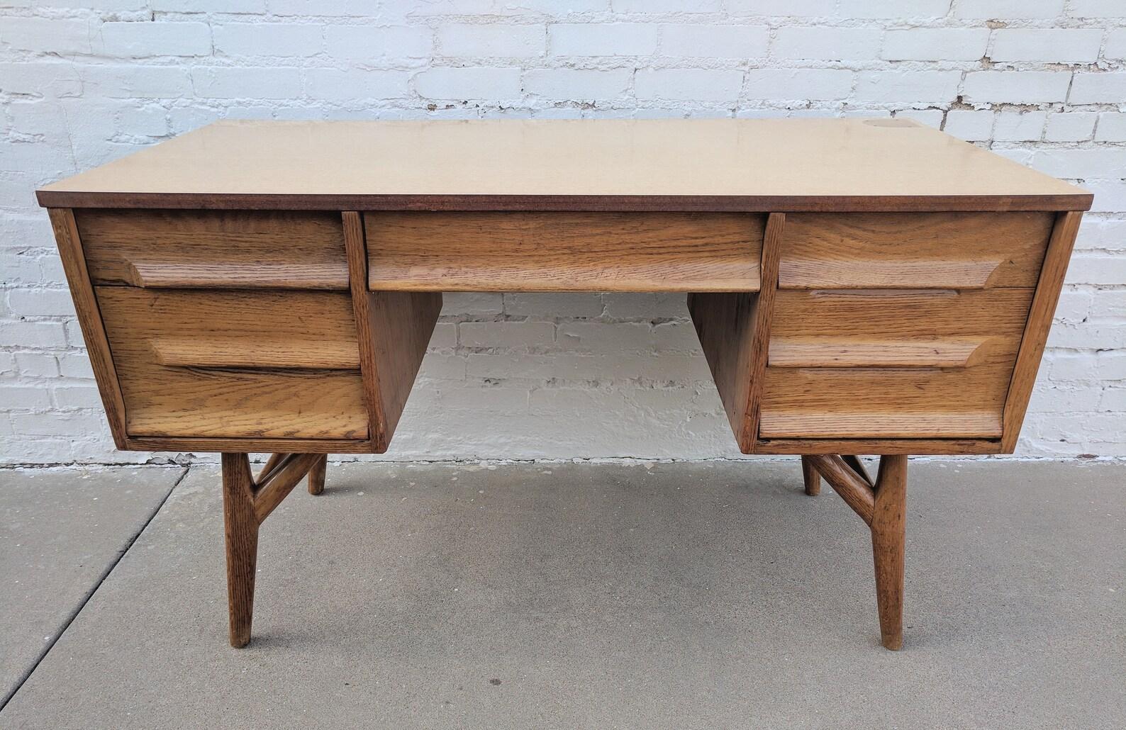 Mid Century Modern Solid Oak Desk with Laminate Top

Good vintage condition with one leg having a portion split away from the bracing screw which leads to some give in the leg.

Additional information:
Materials: Oak
Vintage from the