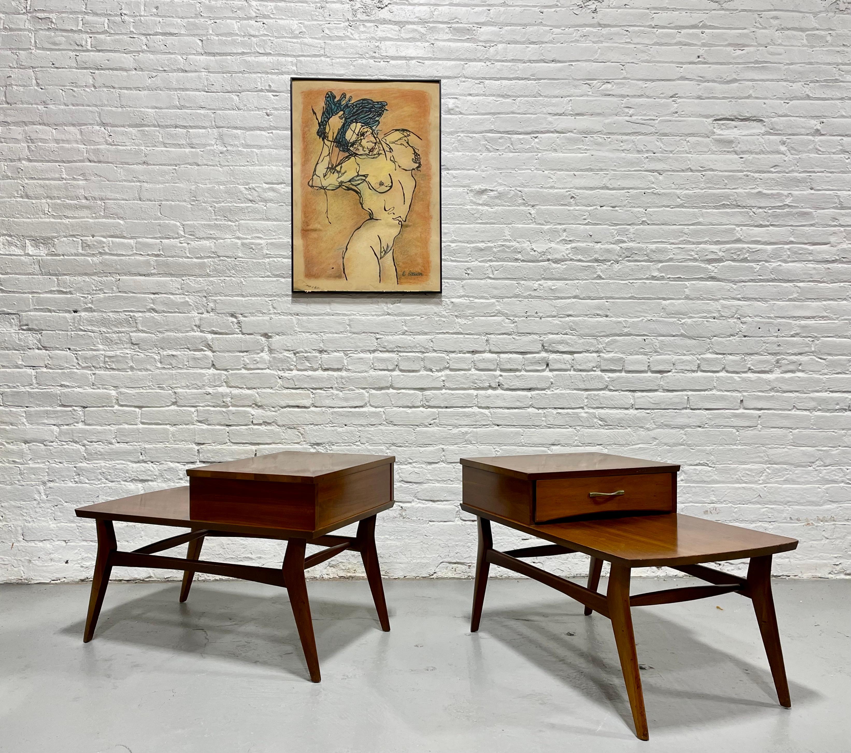 Mid Century Modern Solid Walnut Tiered End Tables by Mersman, c. 1960’s. This solid pair feature incredible wood grains with glorious coloring and tone. Plenty of tabletop space on the upper and lower levels to display magazines, books and even a
