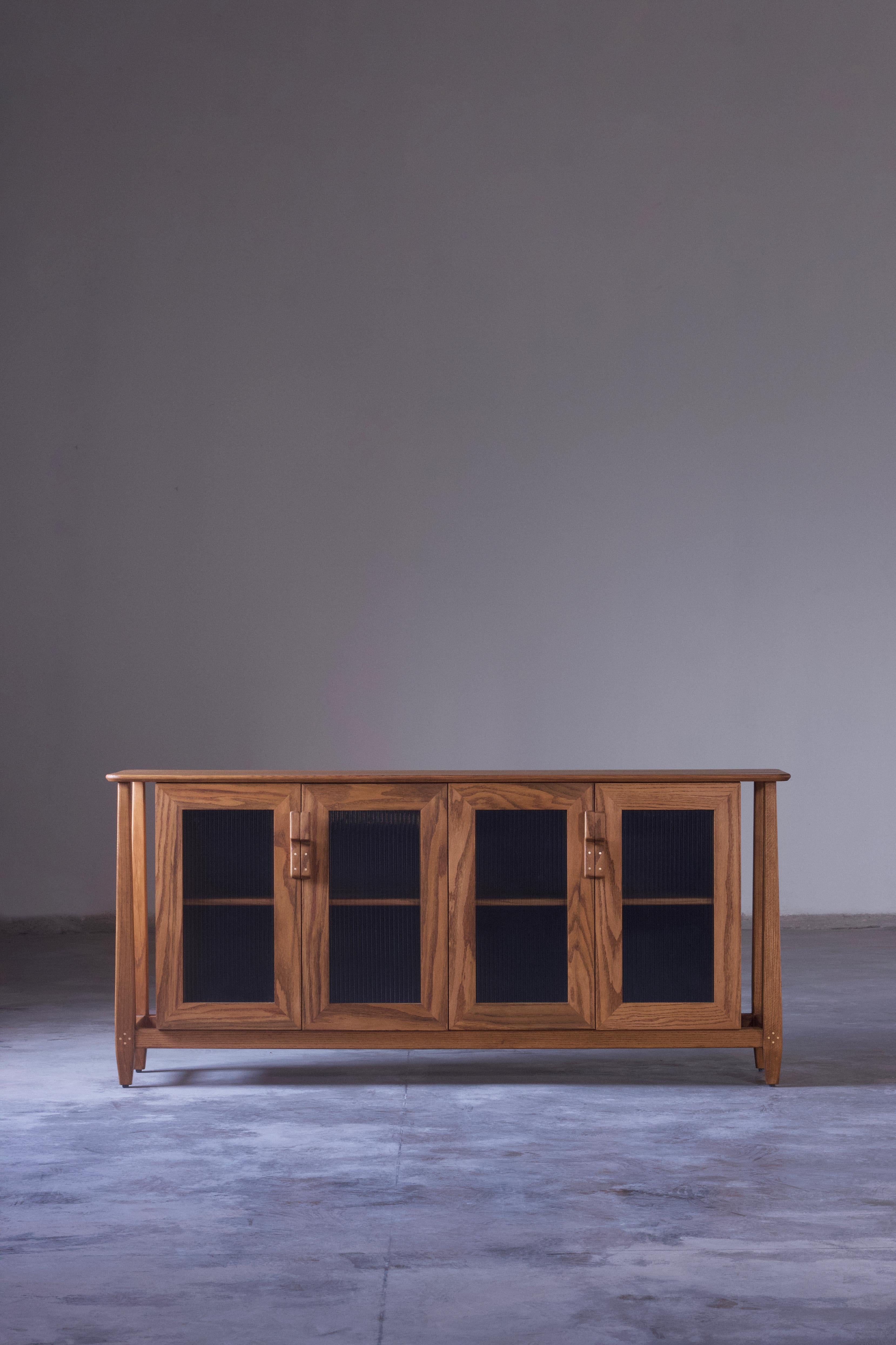 The Dvaara solid wood credenza/sideboard/buffet cabinet is a contemporary interpretation reminiscing traditional Indian architecture and elements. The elegant tapered legs, fluted glass shutters and extended frame of the design brings a visual