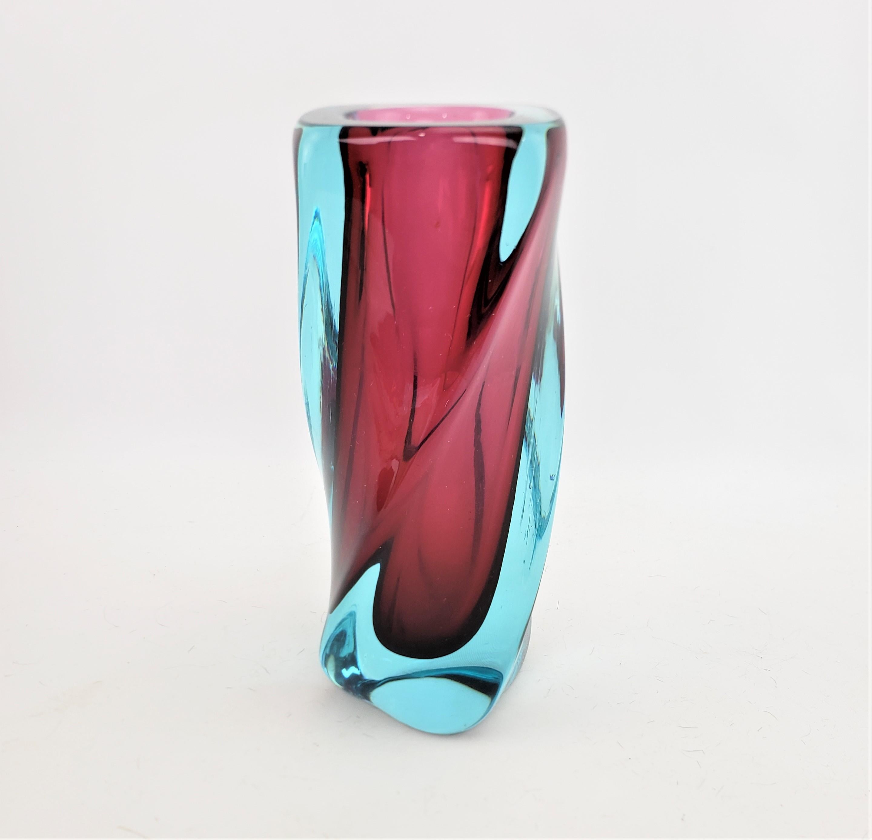 This very well executed art glass vase is unsigned, but presumed to have originated from Italy and dating to approximately 1967, and done in the period Mid-Century Modern style. The vase is done with a heavy aqua blue glass, with a deep red or