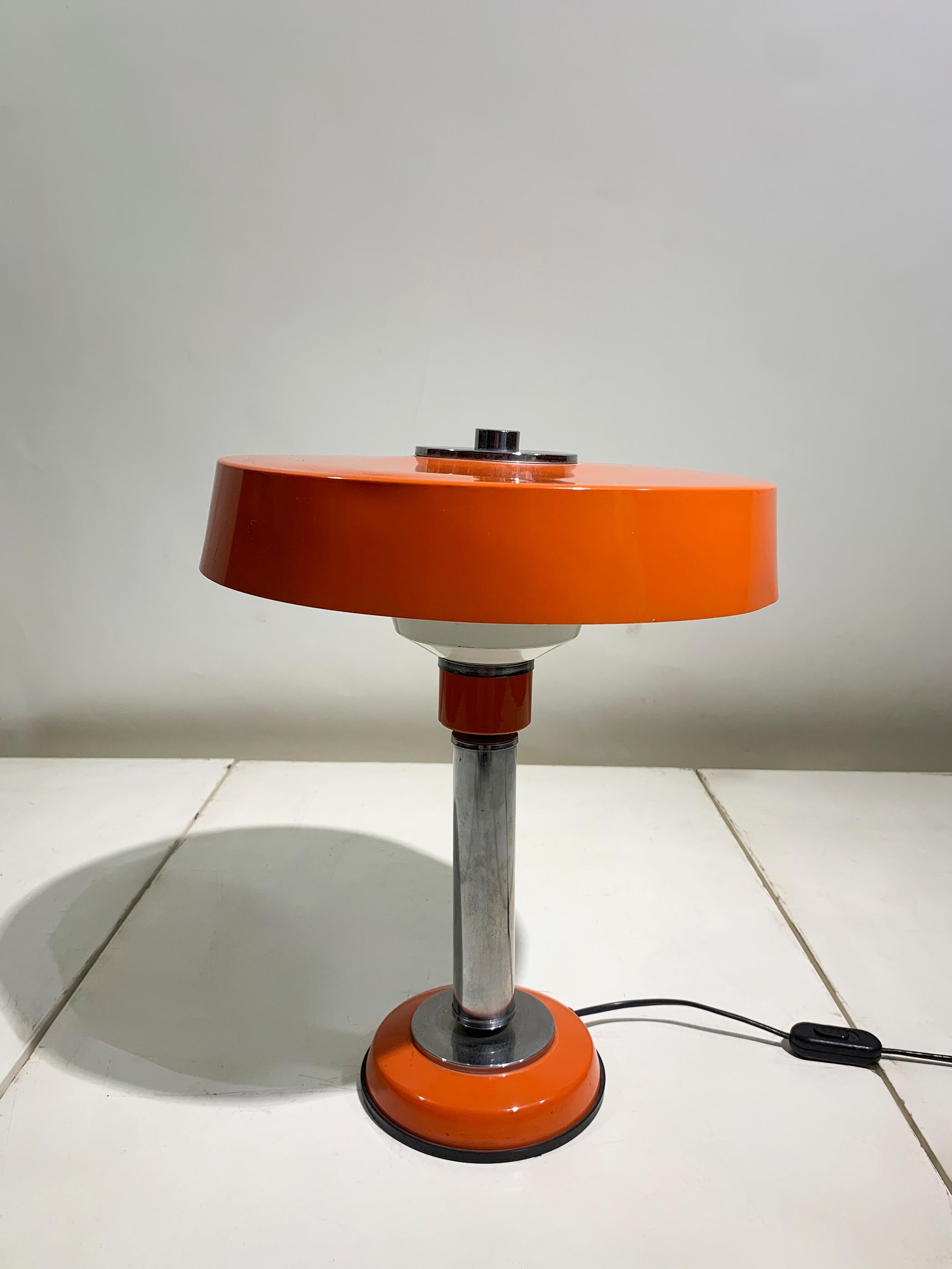 Cette lampe de table dynamique capture le futurisme optimiste des années 1970 avec sa couleur audacieuse et sa forme géométrique épurée. La pièce se caractérise par un abat-jour large et peu profond en forme de soucoupe, d'une couleur orange