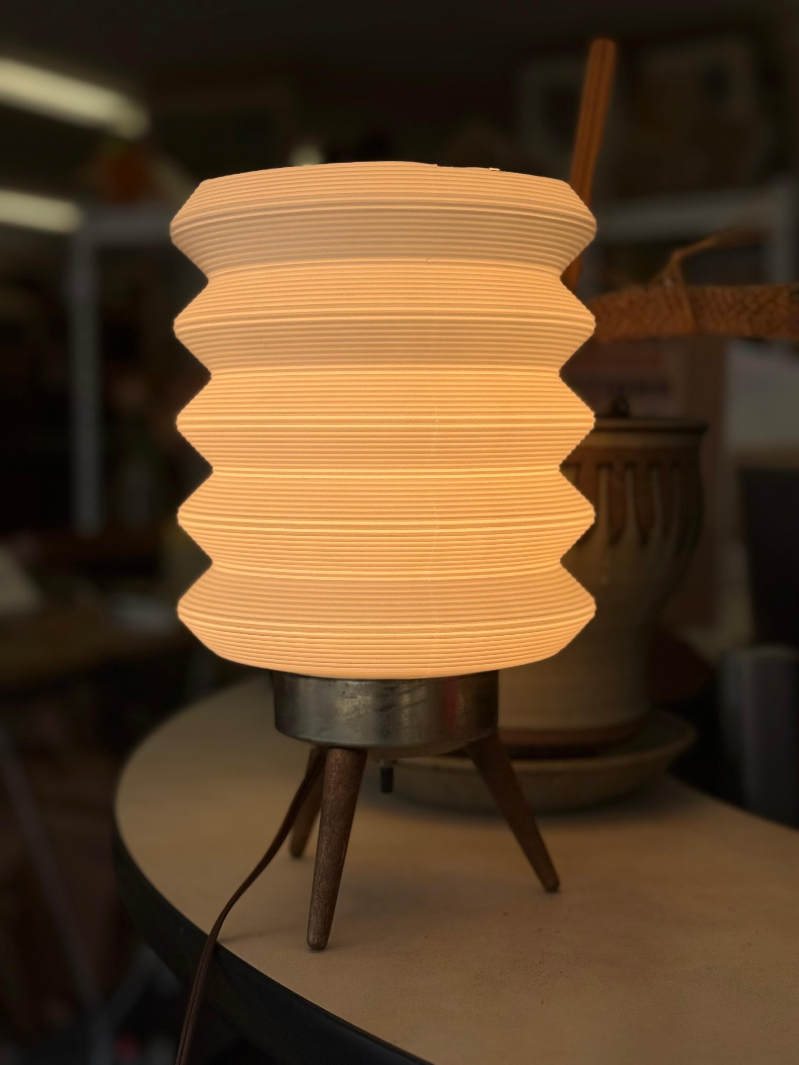 In style of Angelo Lelli, mid-century sculptural table lamp possibly from the 1950s, featuring a wooden tripod body, possibly walnut. The sculptural silhouette showcases elegant curves and a warm natural finish, anchored by a circular patinated