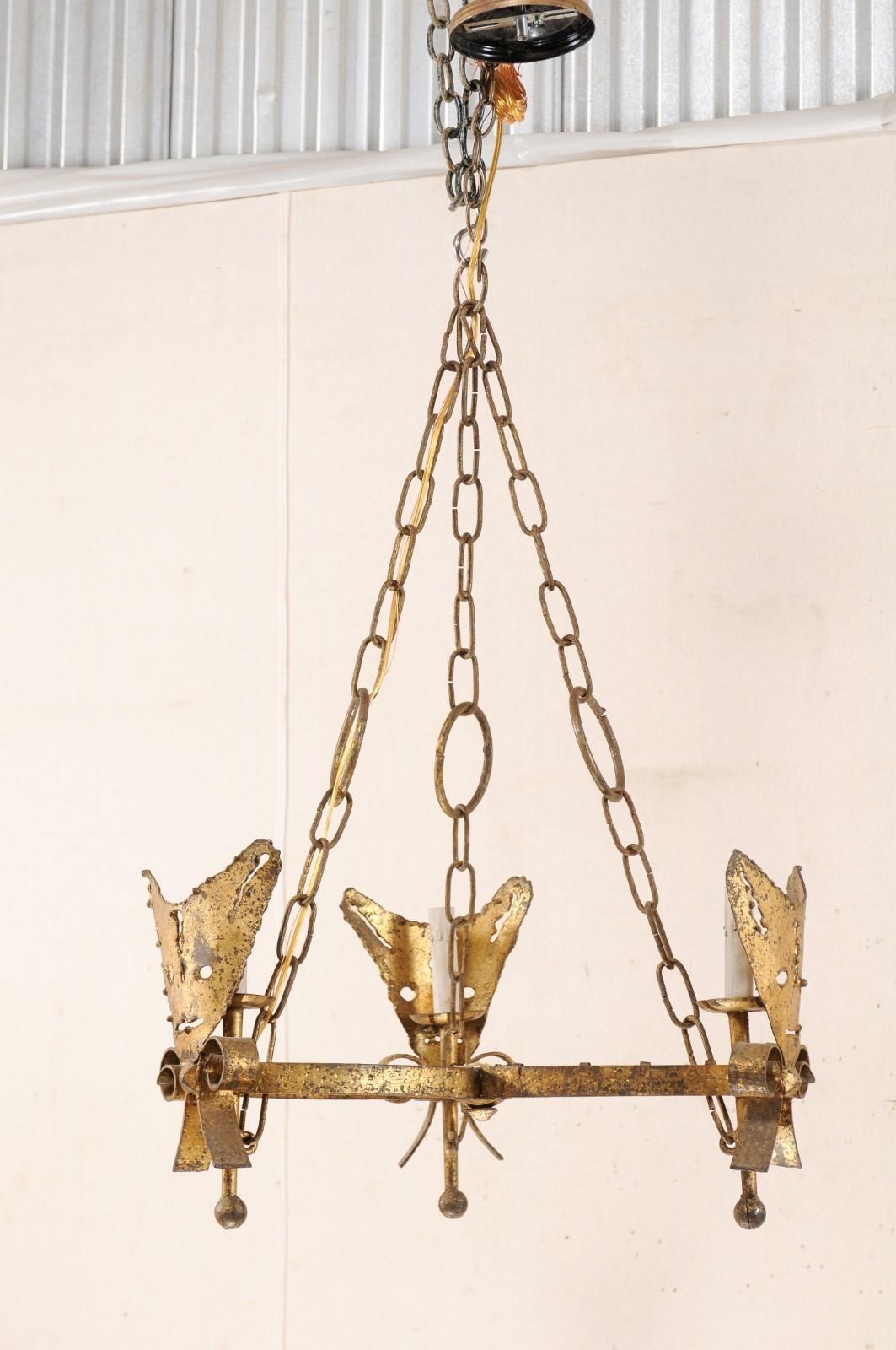 A Spanish Mid-Century Modern three-light iron chandelier in gold color. This modern style hanging light fixture from Spain features three petal-shaped iron bowed arms, jointed together at center, reaching out about the perimeter, embellished with