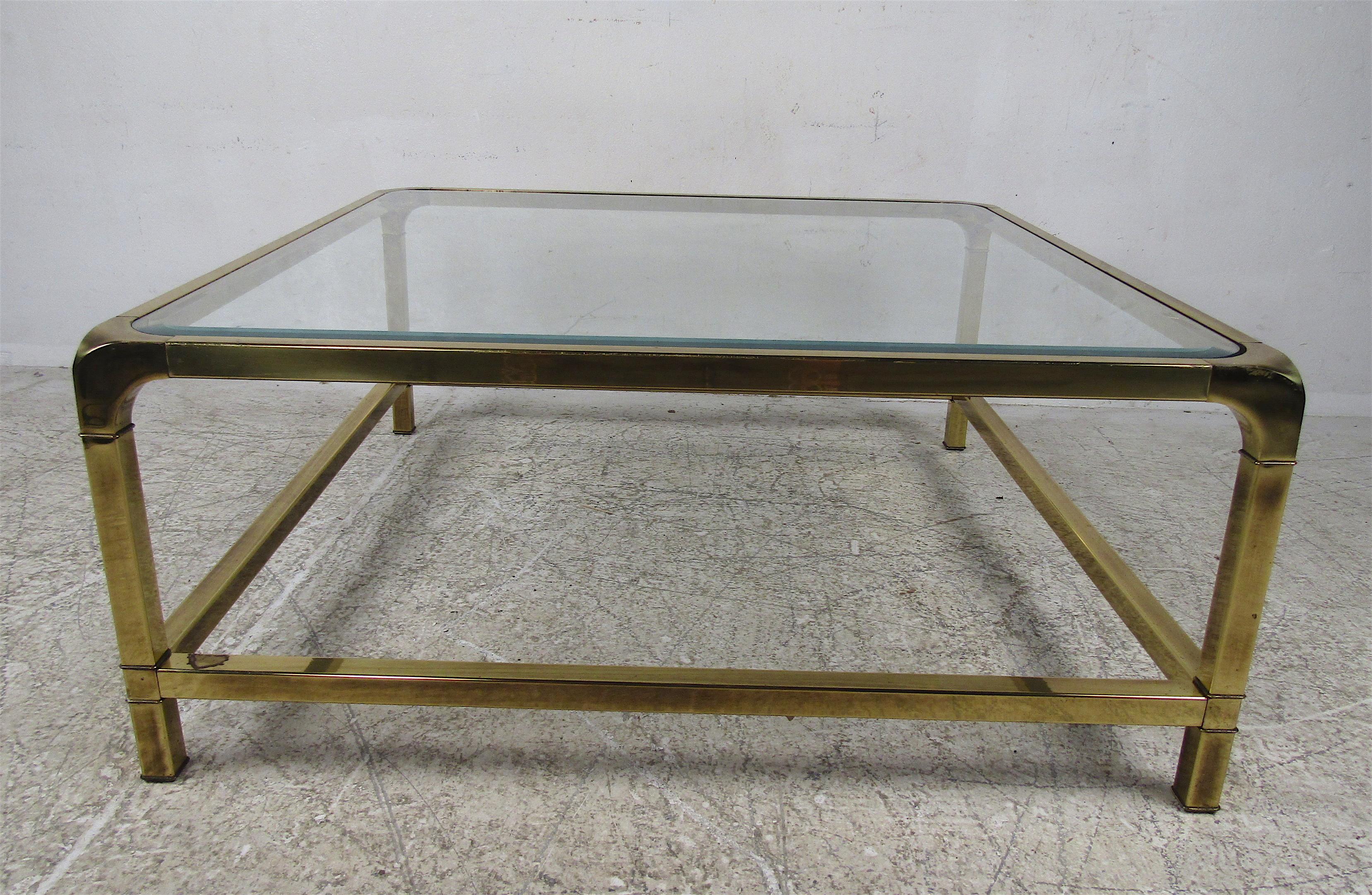 A stunning vintage modern cocktail table with thick beveled glass and a heavy brass frame. Unique design with rounded off edges and four added stretchers along the base for sturdiness. A well-made table that looks great in any home, business, or