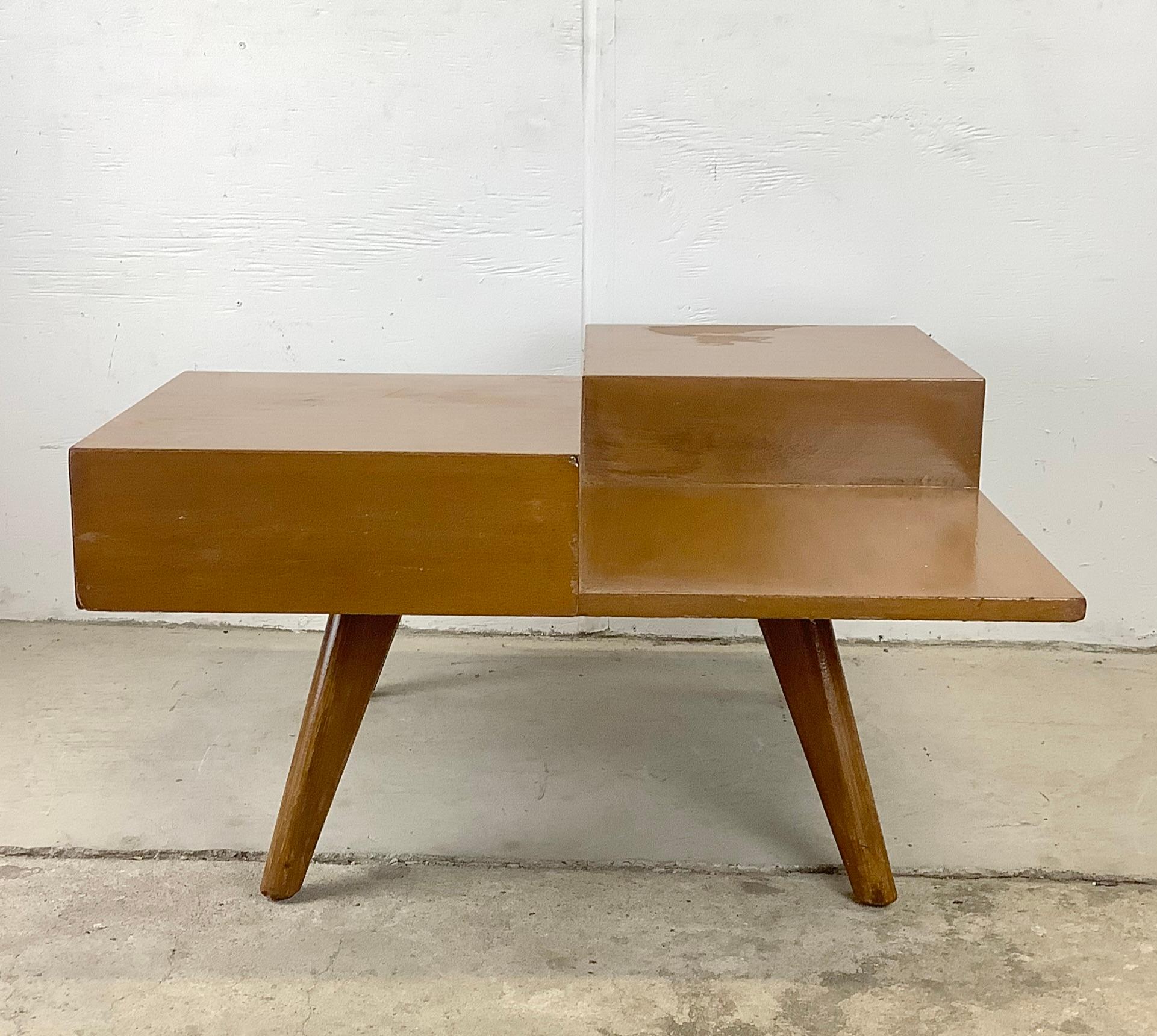 This unique mid-century cocktail table features a striking two tier design with dual pull out drawers for extra storage hidden right in your seating area. Vintage wood finish and sculptural tapered legs add a distinctive mid-century modern style to