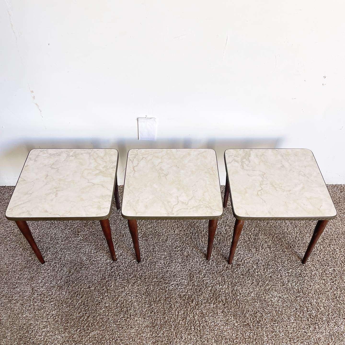 Discover the versatility and elegance of this exceptional set of vintage mid-century modern stacking/nesting tables. With their square wooden legs and faux marble laminate tops adorned with Greek design banding, these tables effortlessly combine
