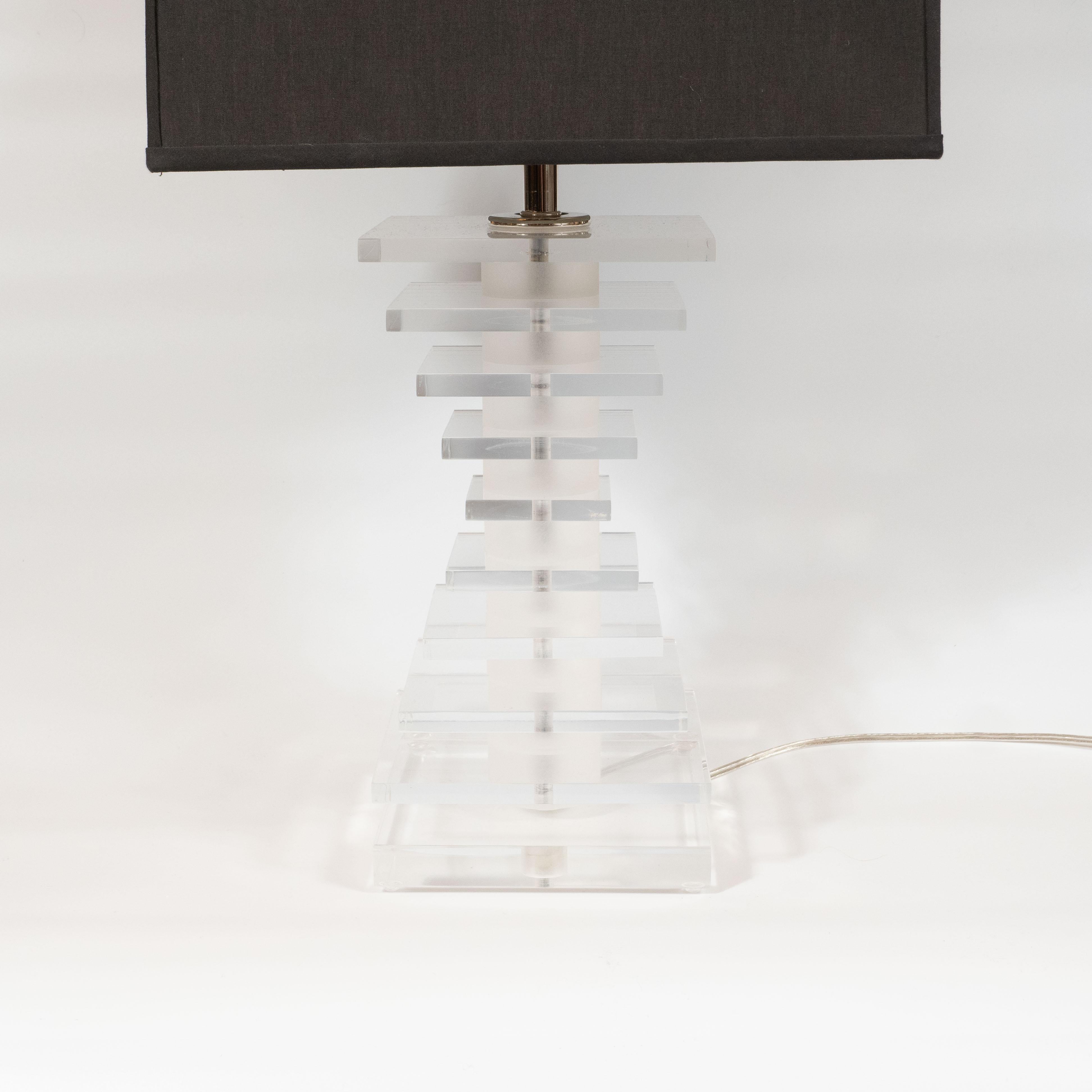 This chic and sophisticated Lucite skyscraper style table lamp was realized in the United States circa 1970. Translucent stacked Lucite panels- alternating with frosted bands in the same material- are stacked to create an hour glass form that is