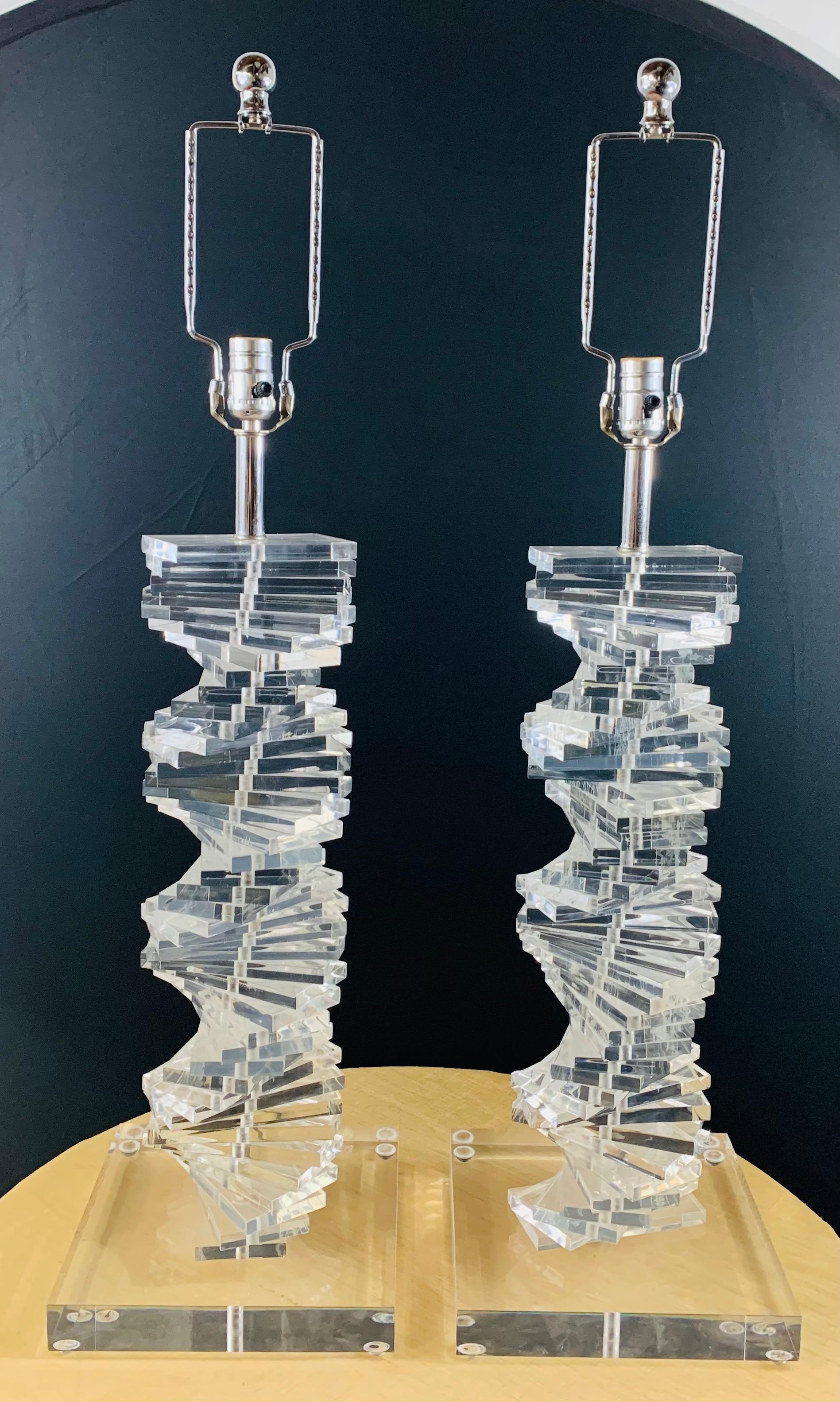 A stunning pair of Mid-Century Modern Lucite stacked Lucite table lamps, in the grand spiral staircase design. Each lamp stands on a square Lucite base. The MCM lamps are a statement period pieces and will light any room while adding style and