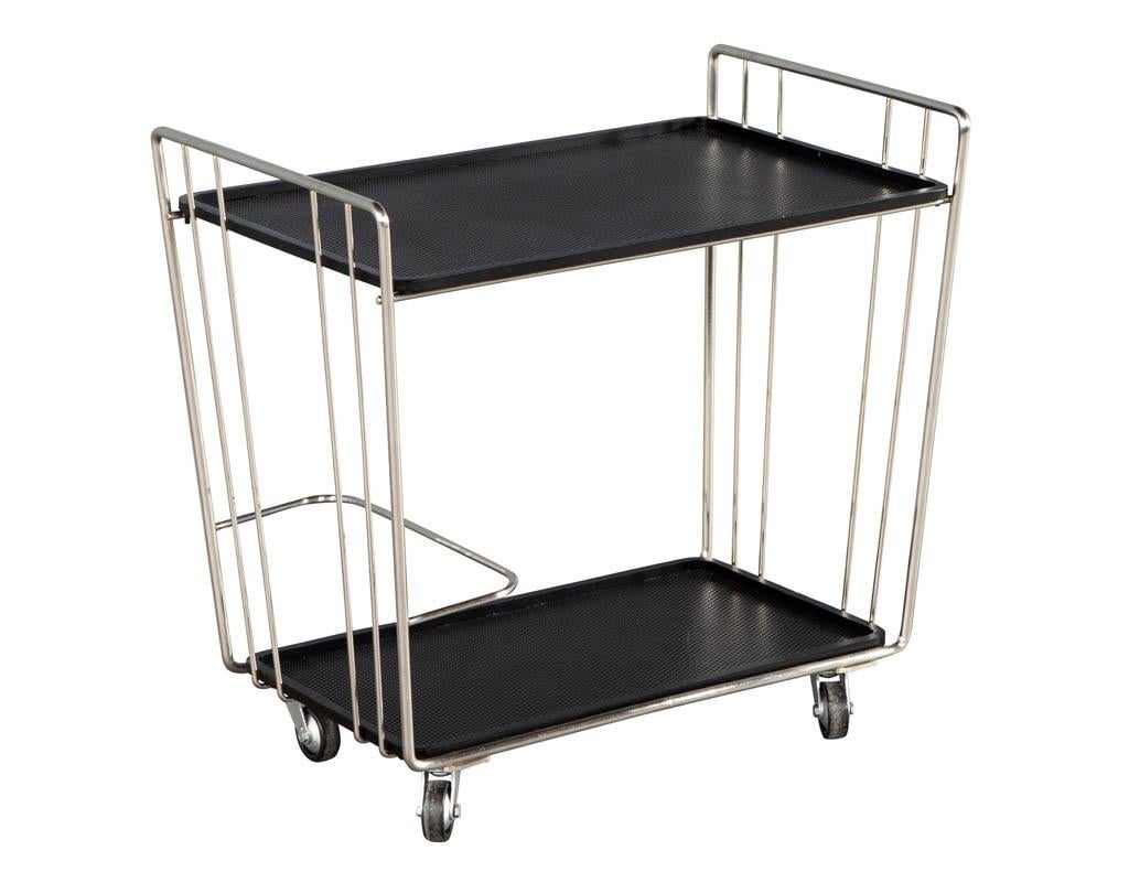 Mid-Century Modern stainless steel bar cart. Unique stainless steel tubular design with black perforated metal shelves. Features curved metal bar to keep bottles secure. American, circa 1970s. In restored condition with minor wear consistent with