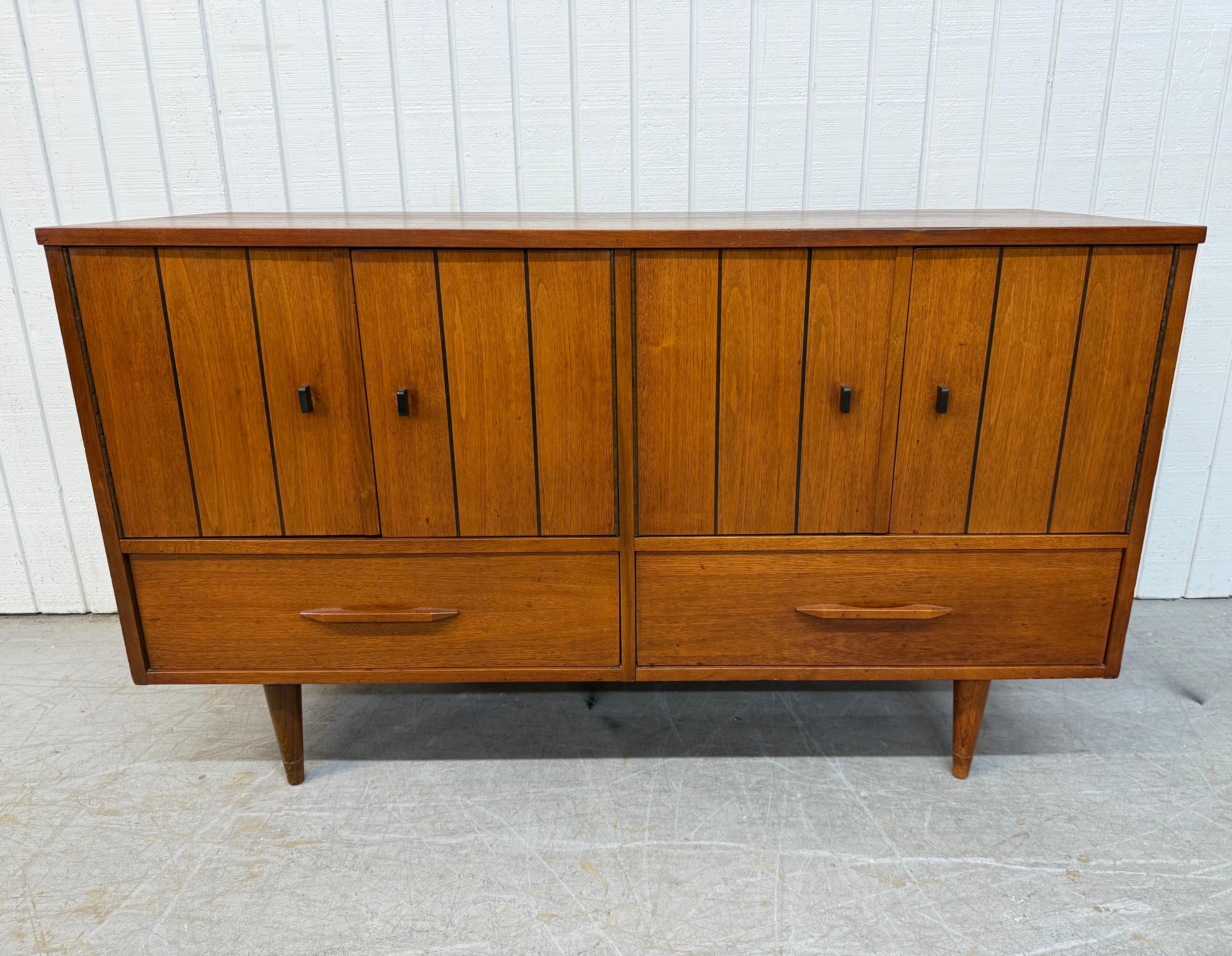 This listing is for a Mid-Century Modern Stanley Walnut Sideboard. Featuring a straight line design, four doors with black pulls that open up to storage space, two drawers with sculpted wooden handles, black pin stripes, modern legs, and a