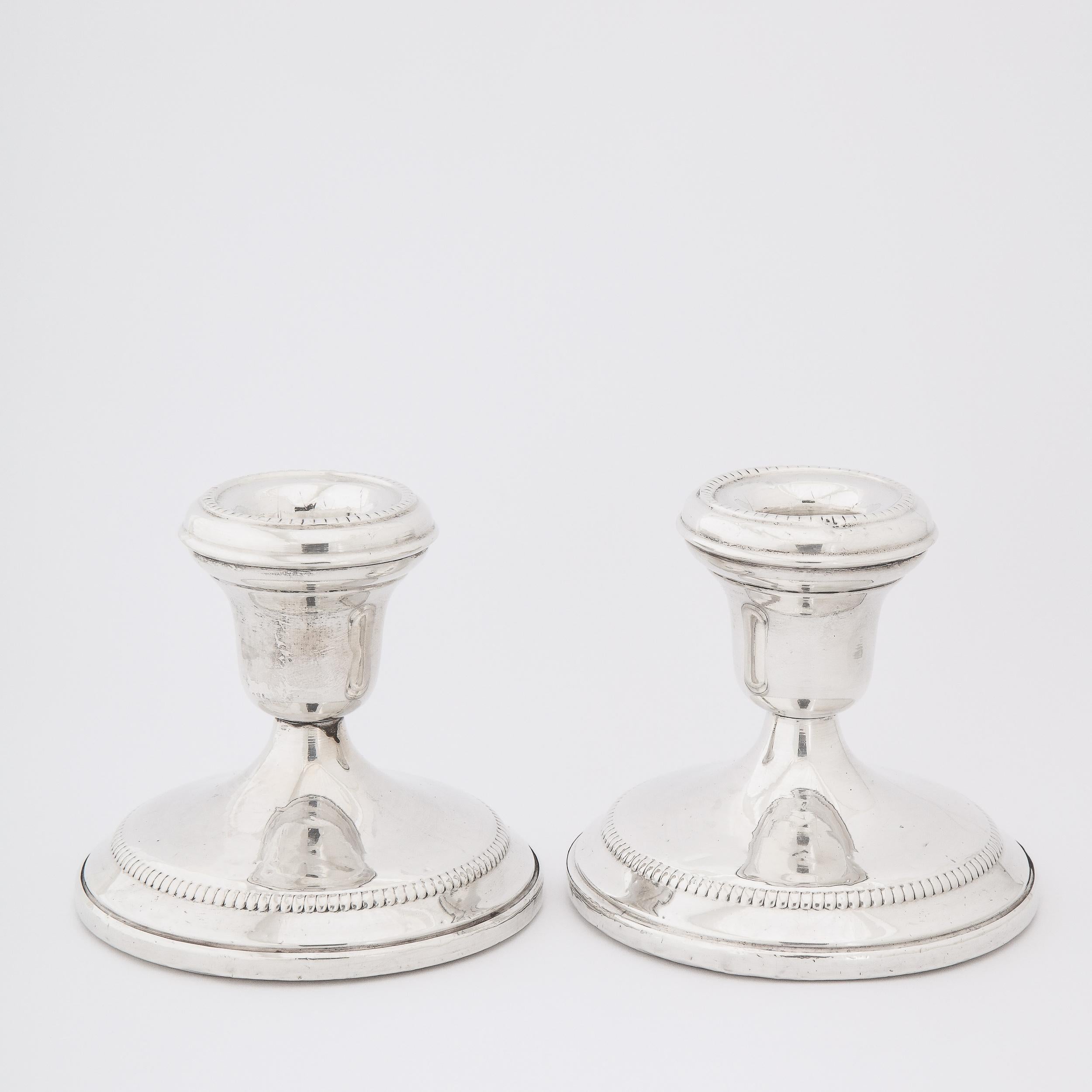 This refined pair of Mid-Century Modern candlesticks were realized in the United States, circa 1960. They feature circular bases that taper upwards to bobeches of the same form- all in lustrous sterling silver. Additionally, there is beaded