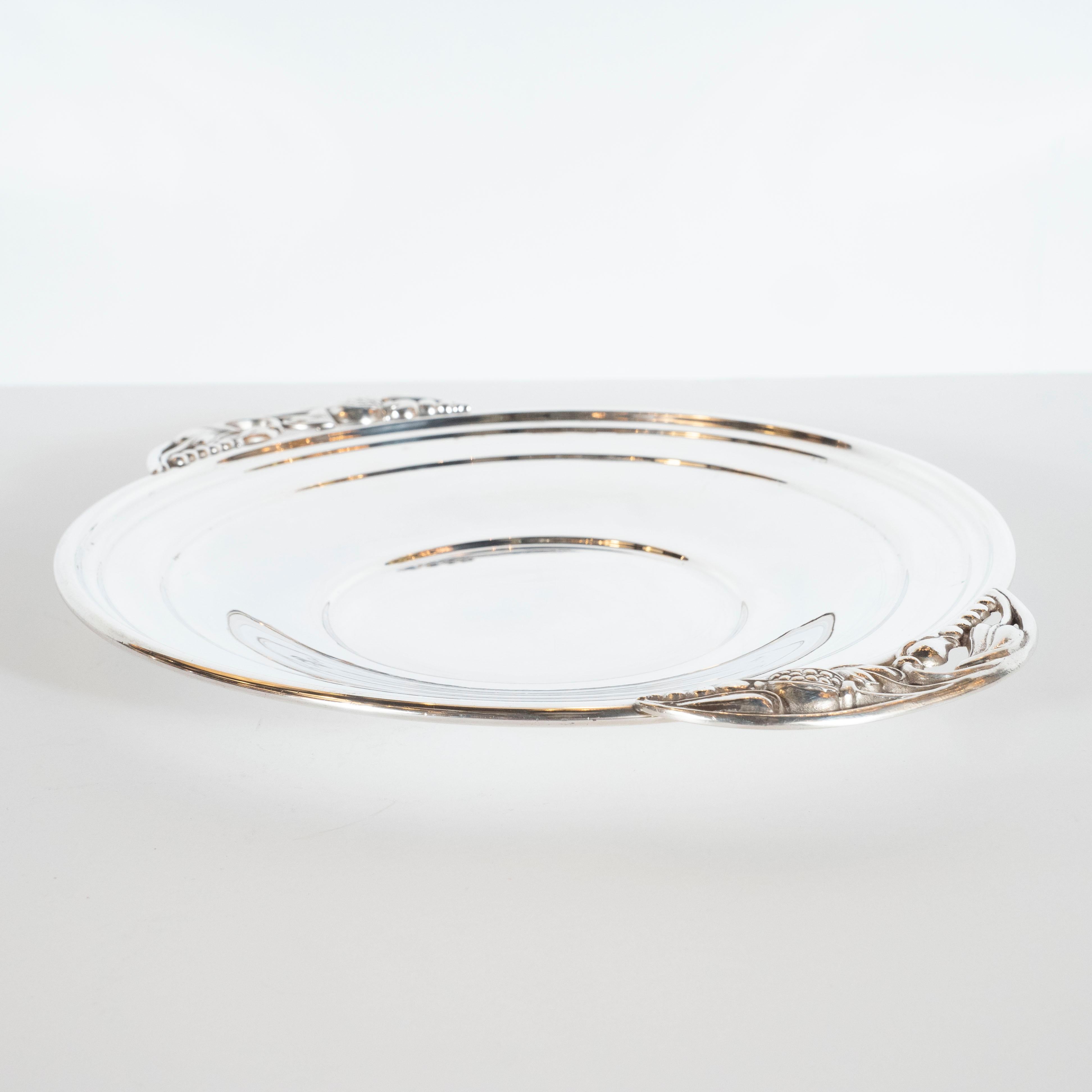 This beautiful sterling silver decorative tray was realized in Great Britain, circa 1950. It features a circular centre with rounded scalloped sides that offer stylized grape and vine detailing in the interstices between the adjoining sides. The