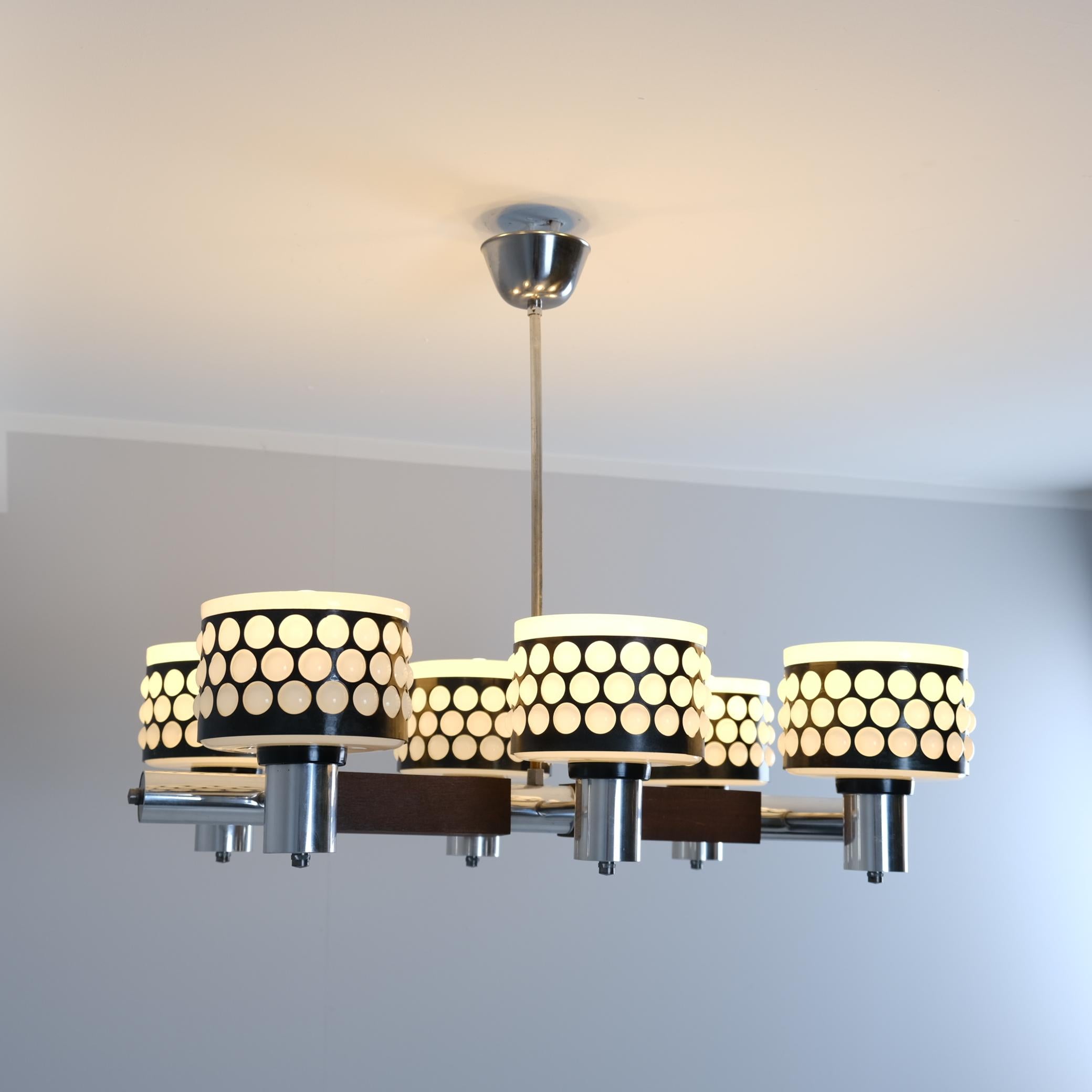 Un pendente da soffitto modernista di Stig Lindström, prodotto da Lival Oy in Finlandia a metà degli anni Sessanta. La sospensione è dotata di sei lampadine con paralumi in vetro lattiginoso e metallo su una base cromata e in teak. Un design che sta