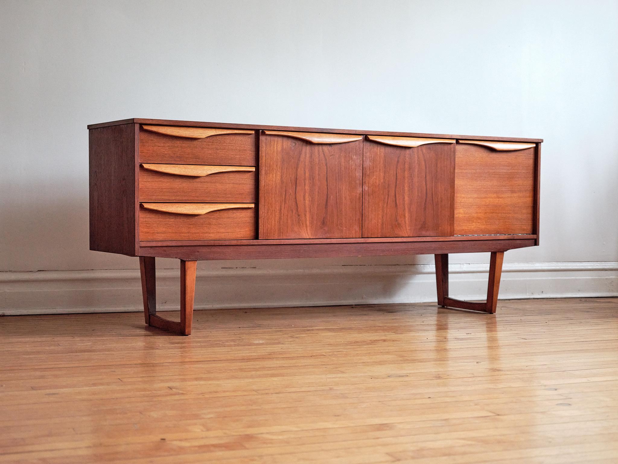 Mid-Century Modern teak wood sleigh leg credenza.
Just imported from England to Chicago.
Made by Stonehill Furniture.
Stunning book-matched woodgrain across the front.
Refinished light wood handles.
Center features double cabinet doors.
One