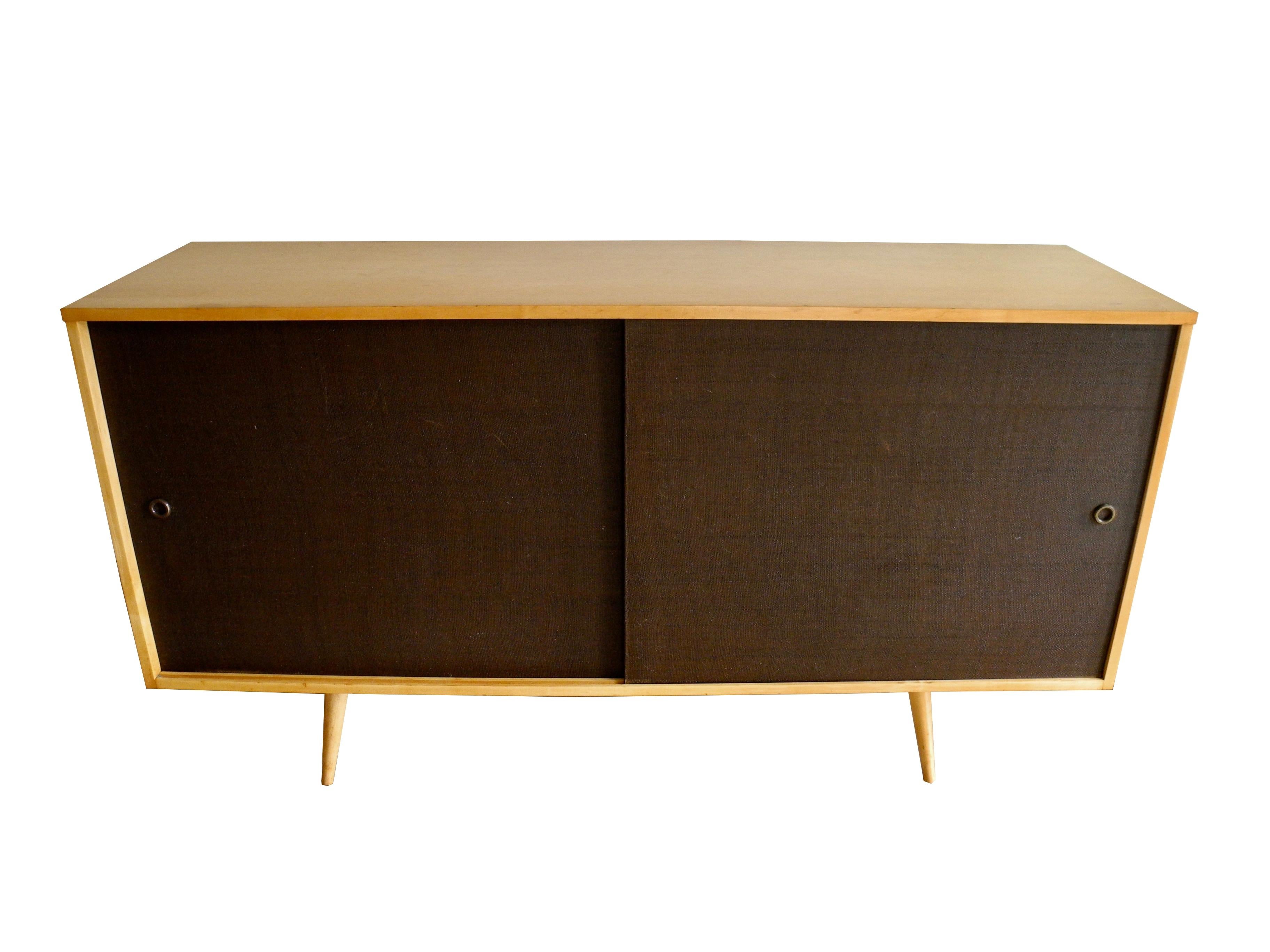 This well known Paul McCobb sideboard is made with solid maple wood. Equipped with four drawers and a shelf. The panel doors conveniently slide from side to side for easy access. The conical legs screw into wood cleats underneath the case. The